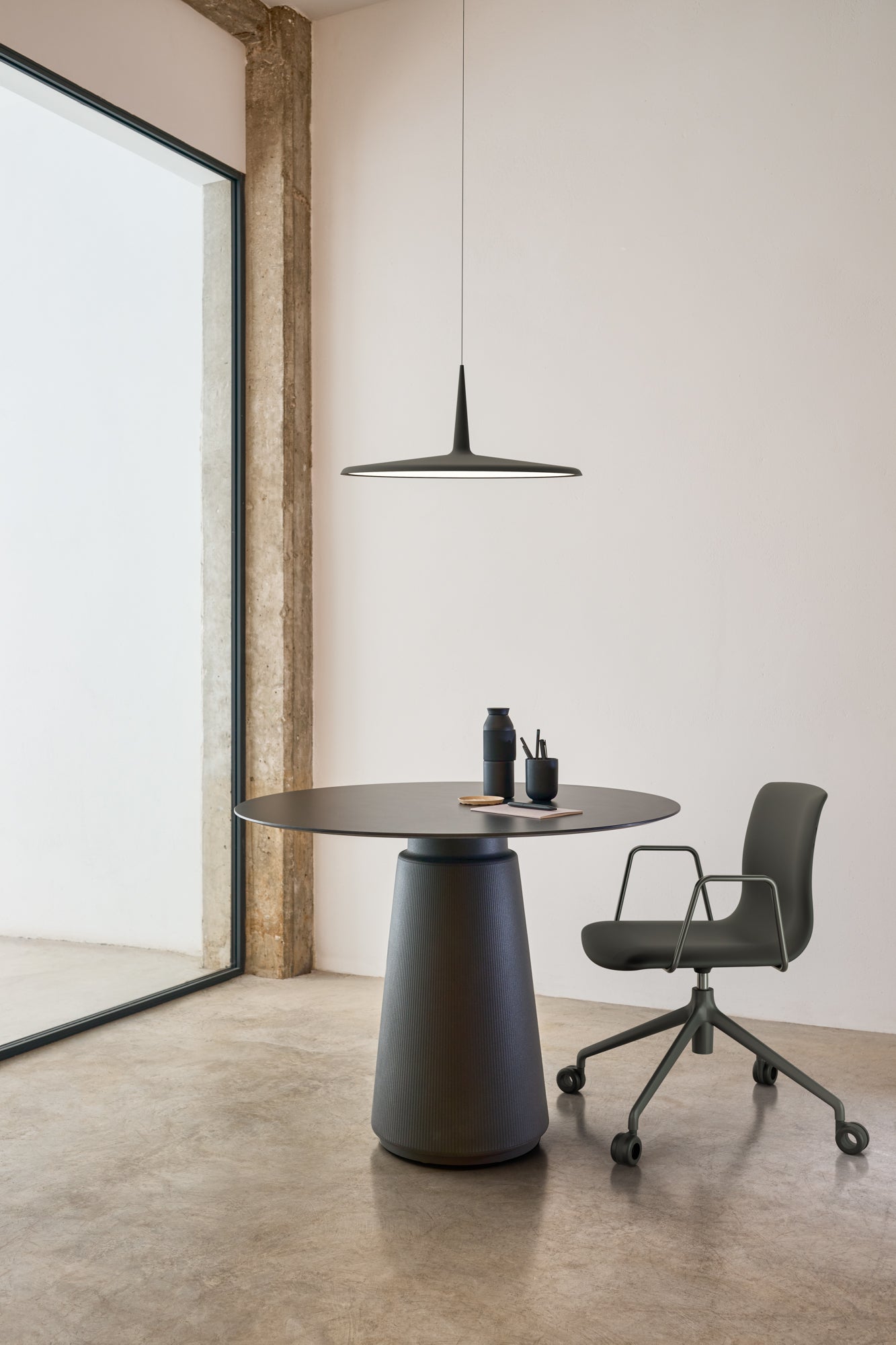 Modern office setup with a round table and chair in a minimalistic room.
