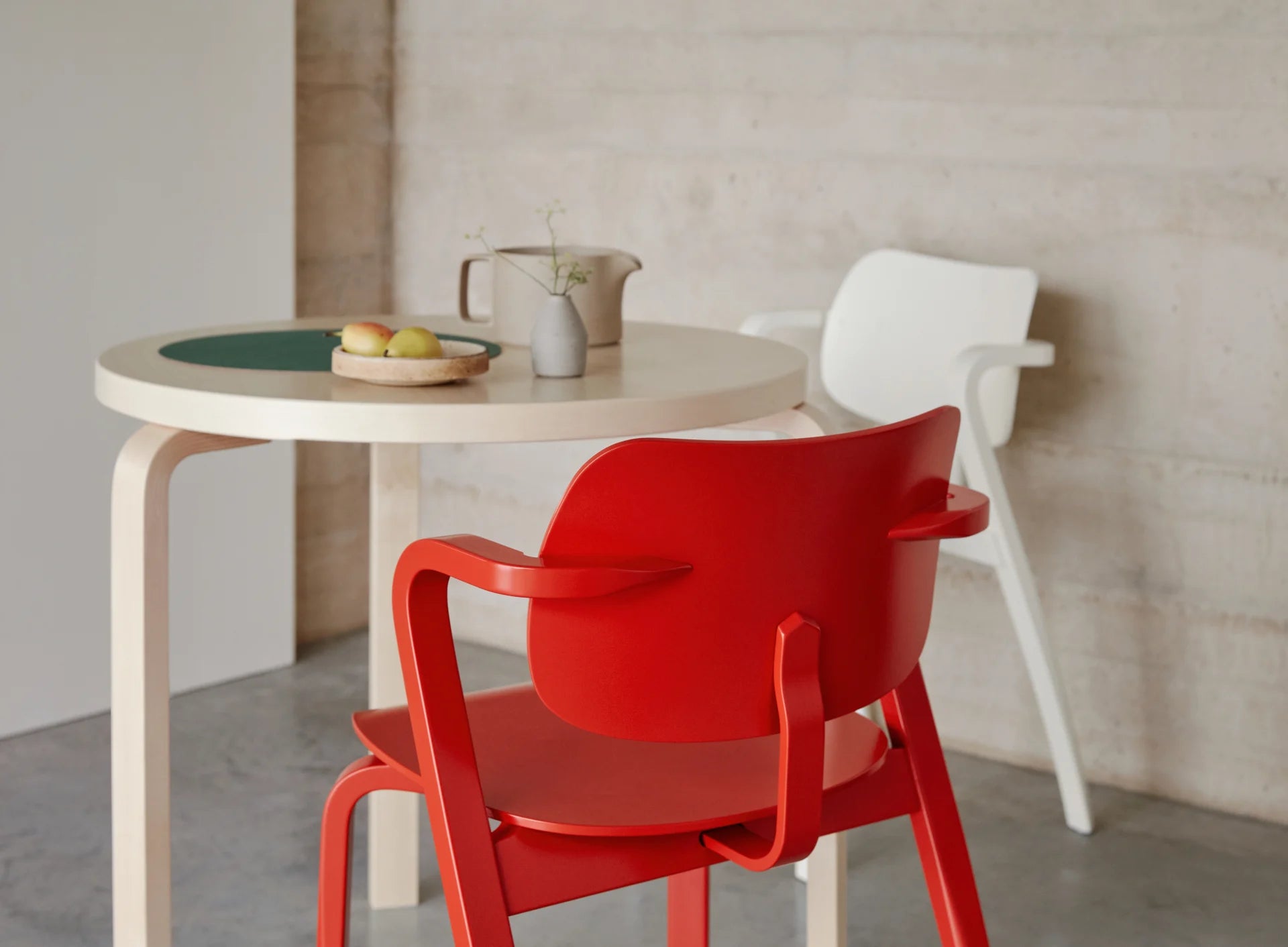Round table with a red chair and a white chair against a neutral wall.