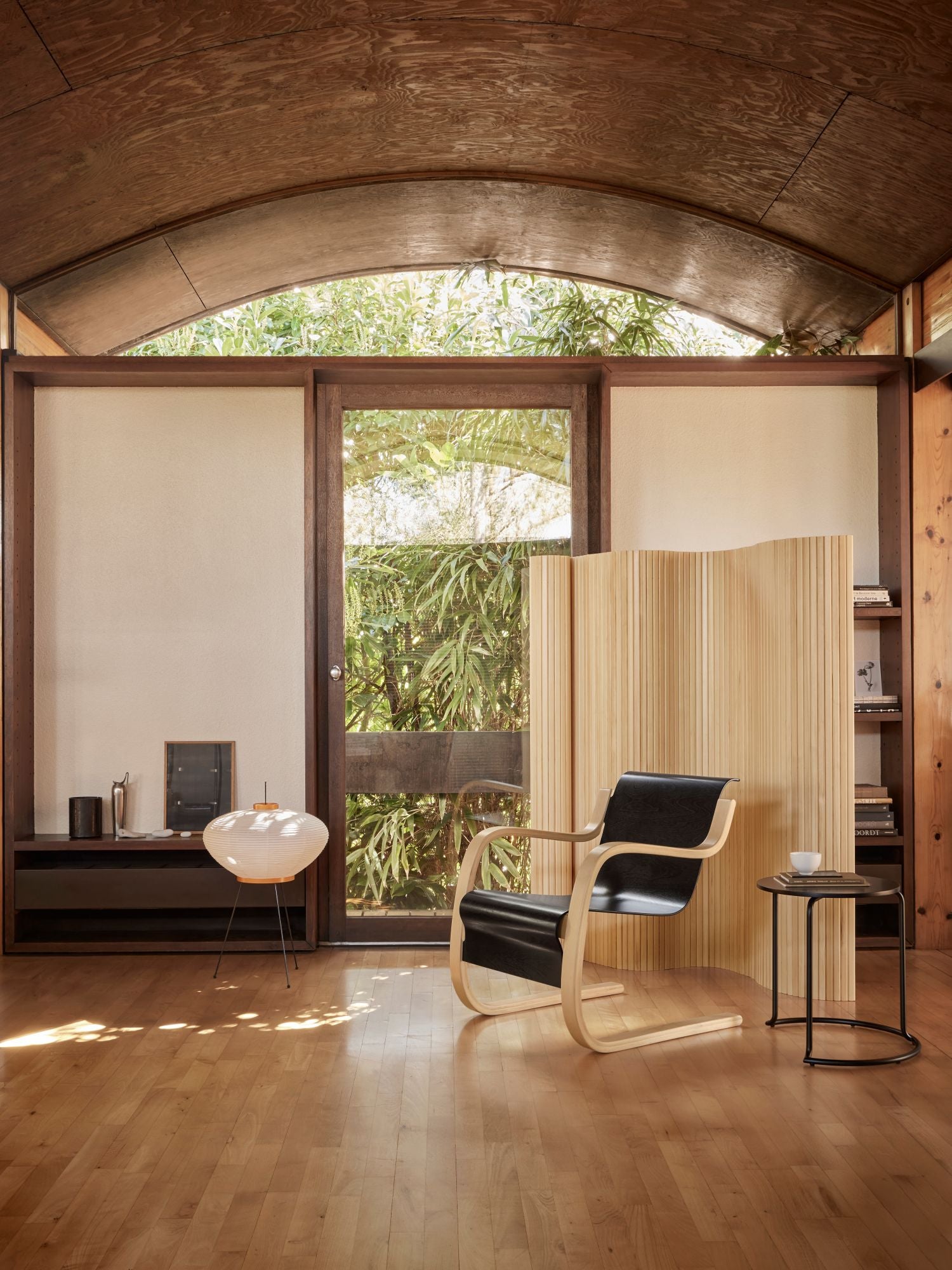 Modern interior with a chair, table, and large window showing greenery outside.