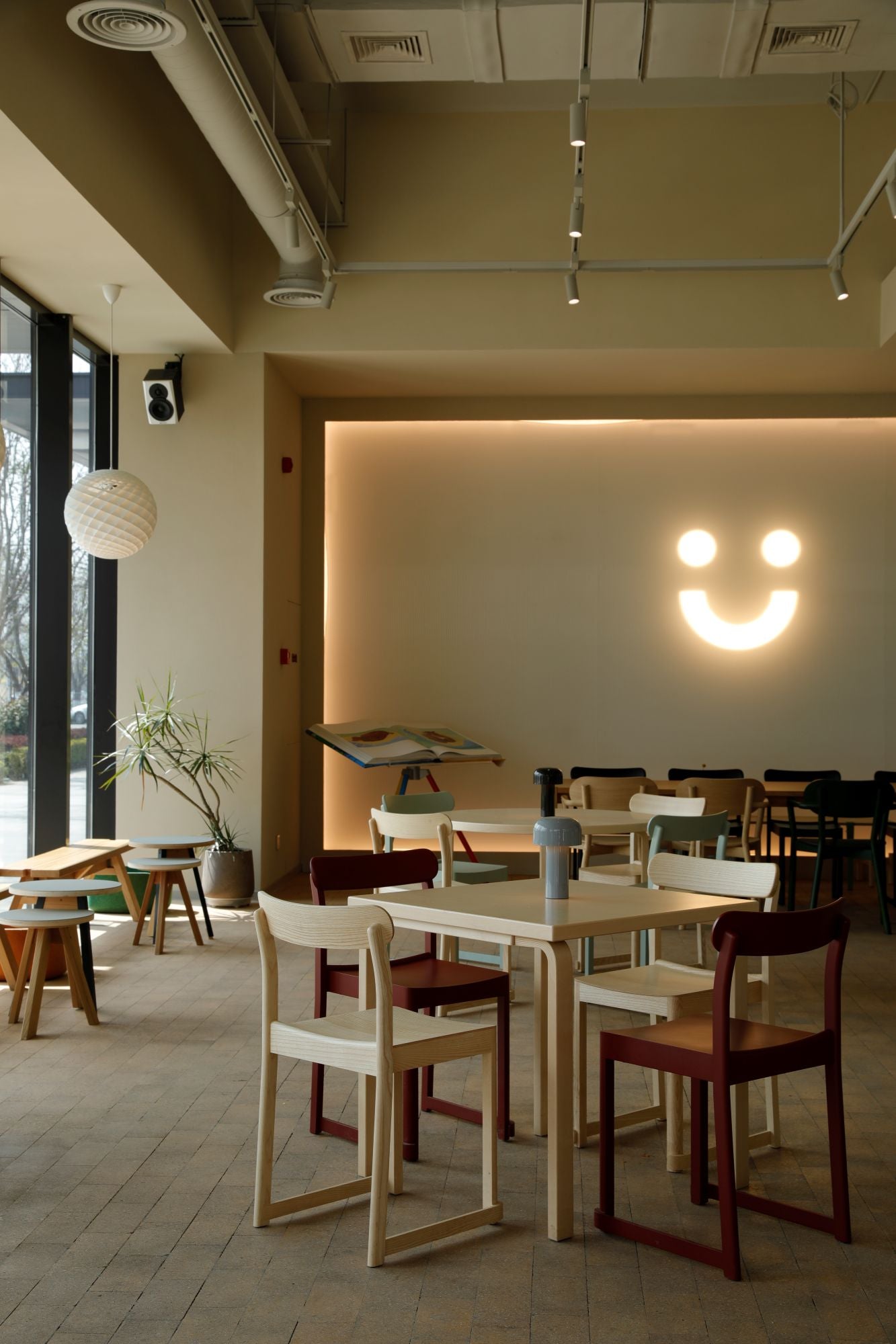 Modern restaurant interior with tables, chairs, and a decorative light fixture shaped like a smiley face.