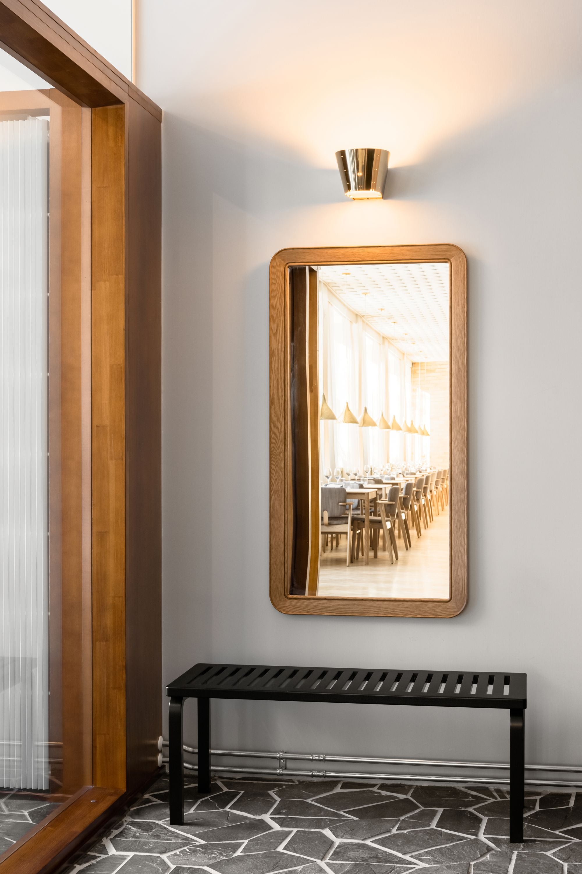 Rectangular mirror with wooden frame on a wall above a black bench.