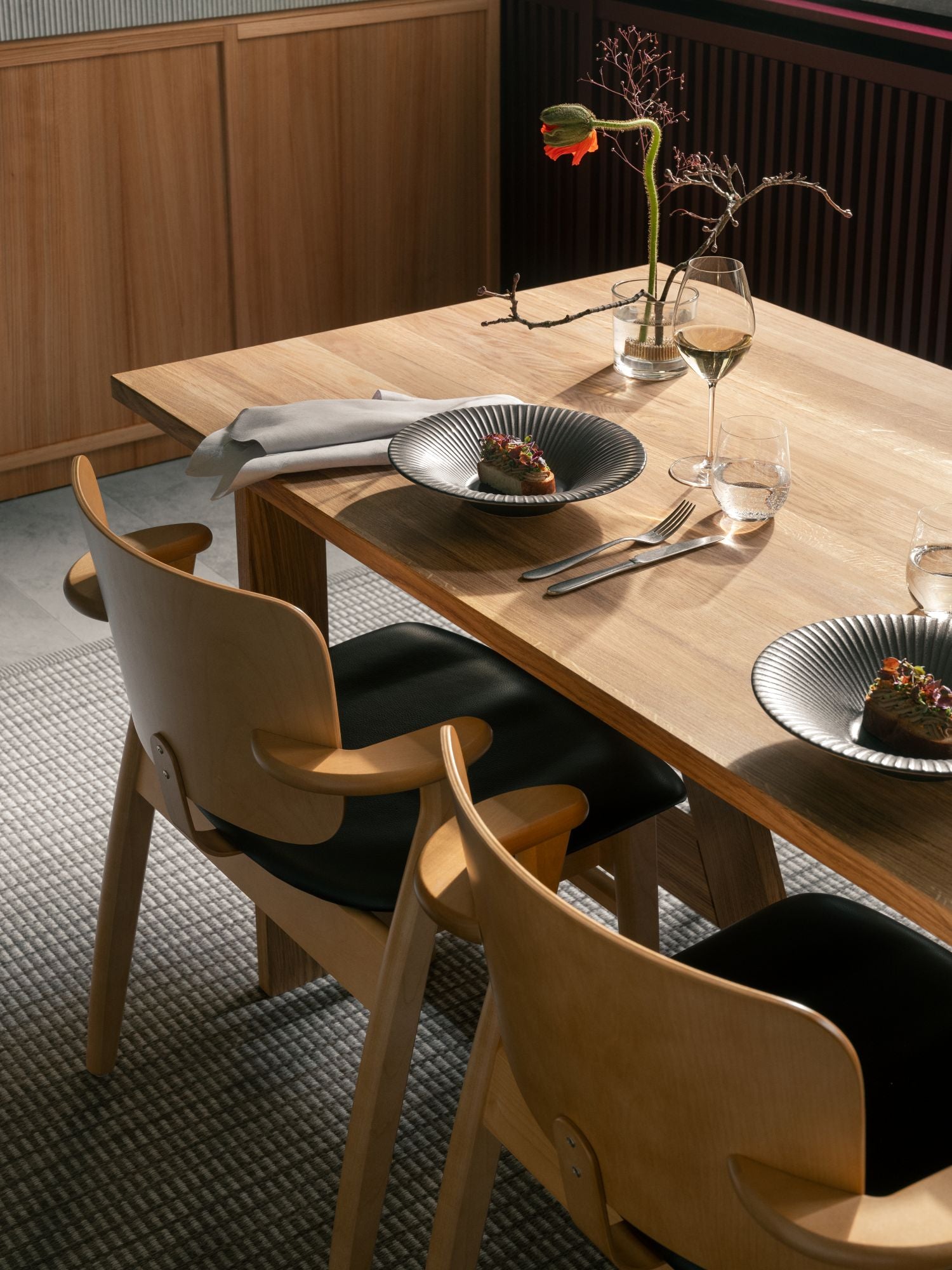 Dining table set with plates, cutlery, and glasses in a modern interior setting.