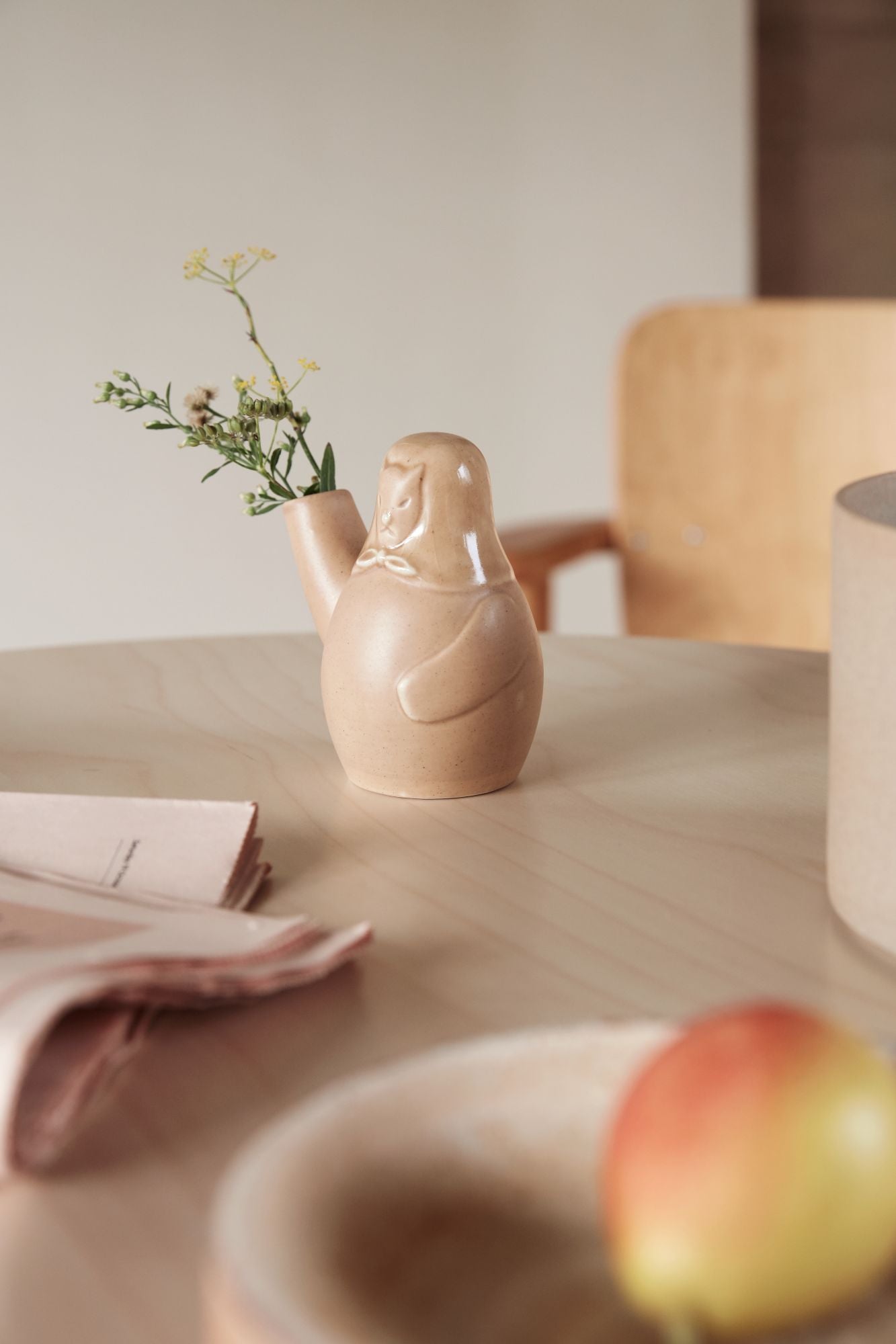 Decorative teapot on a wooden table with a bowl of fruit and a vase in the background.