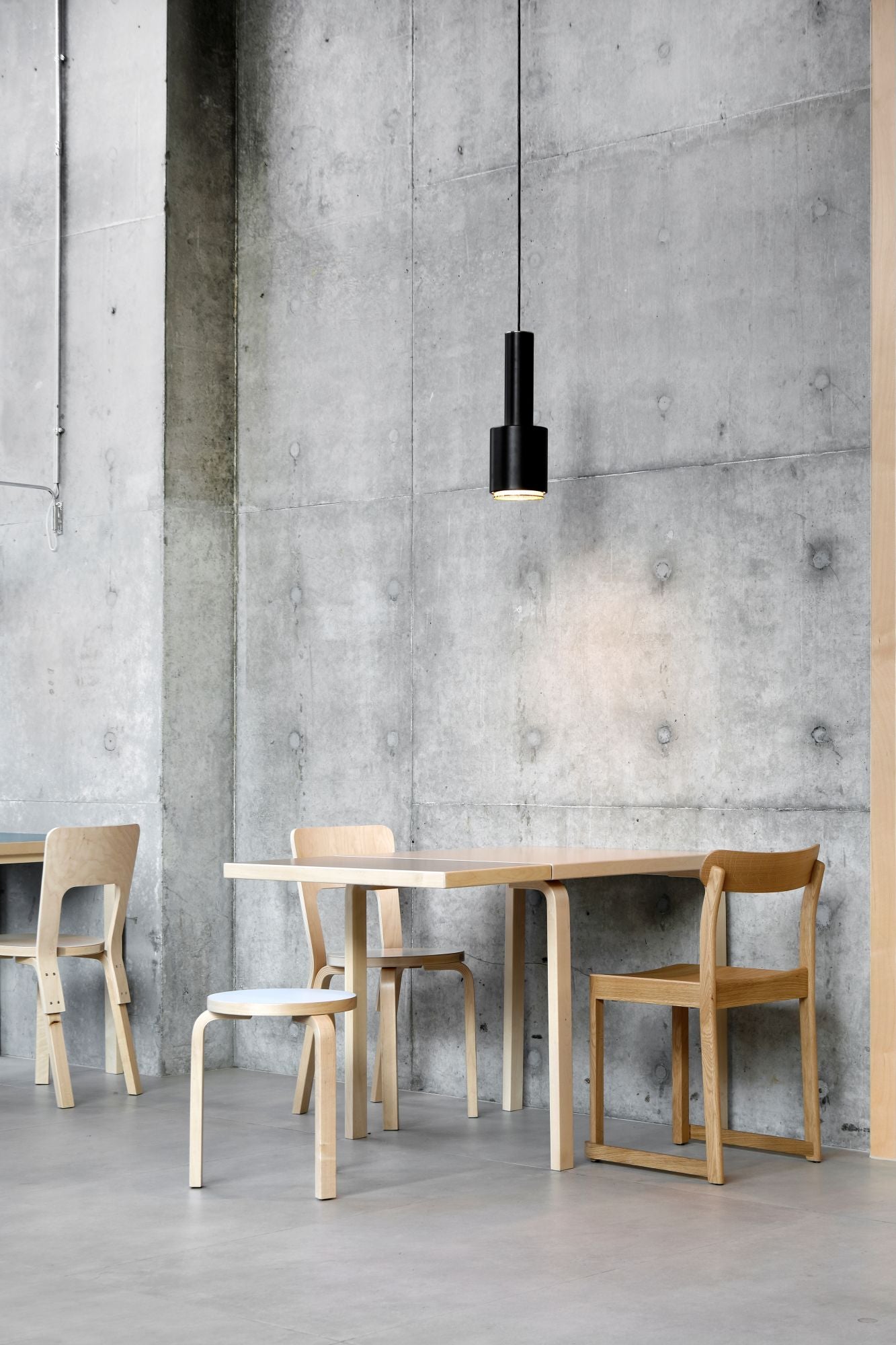 Modern dining area with wooden table and chairs against a concrete wall.