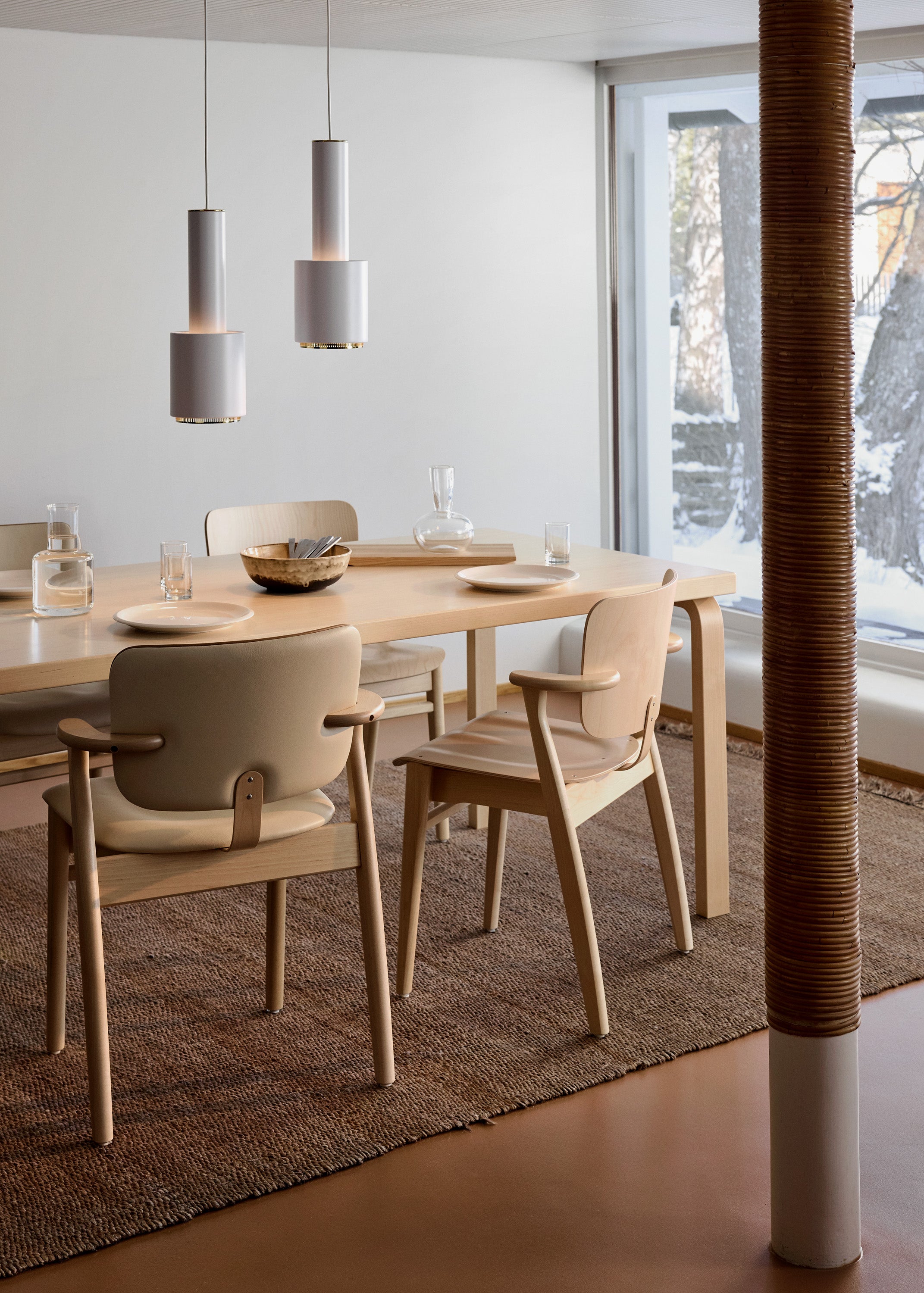 Modern dining area with wooden table and chairs, pendant lights, and large windows.