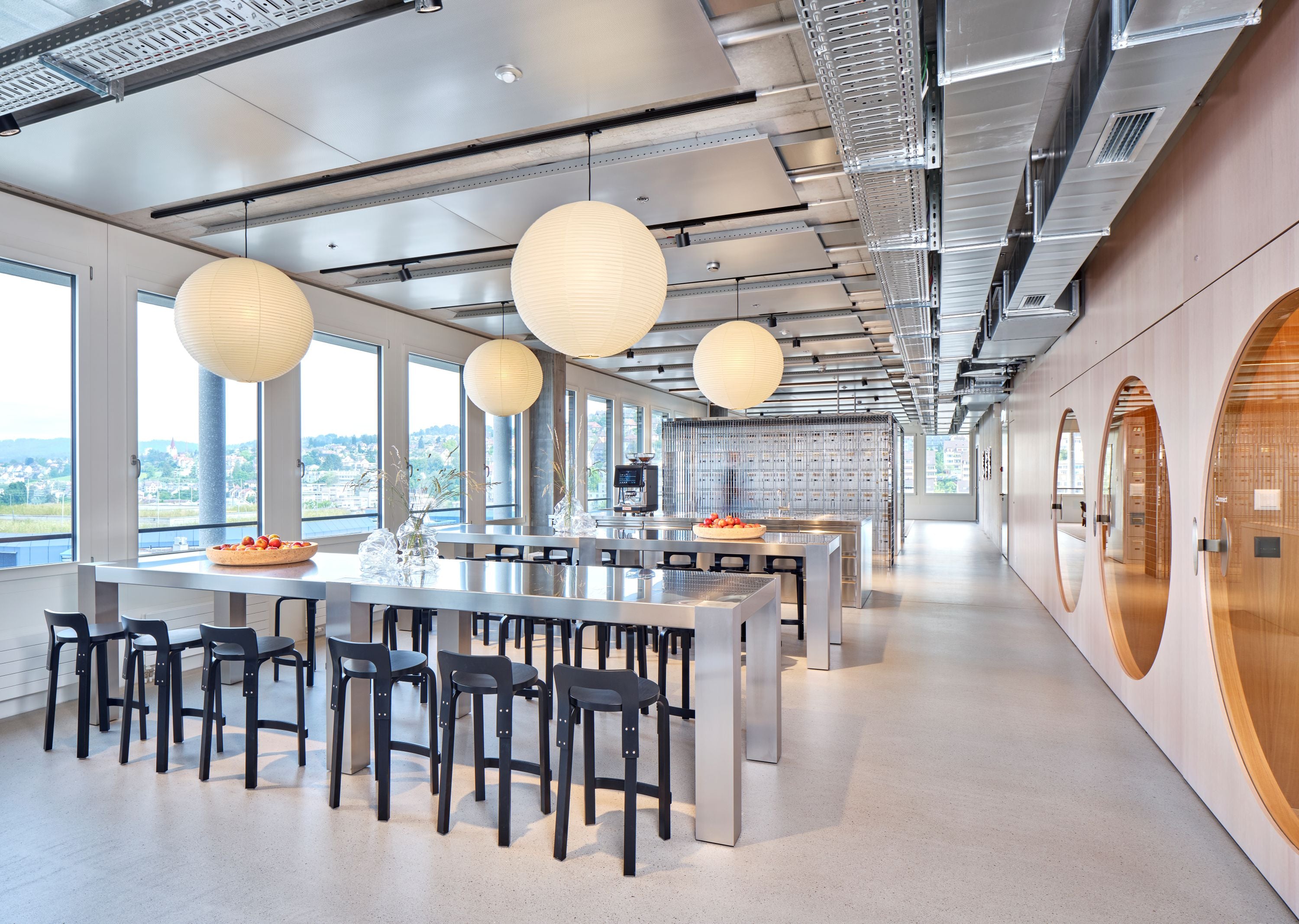 Modern office cafeteria with long tables, chairs, and large windows.