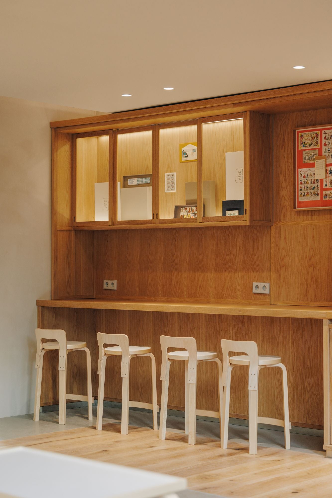 Wooden bar with stools against a wall with cabinets and framed pictures.