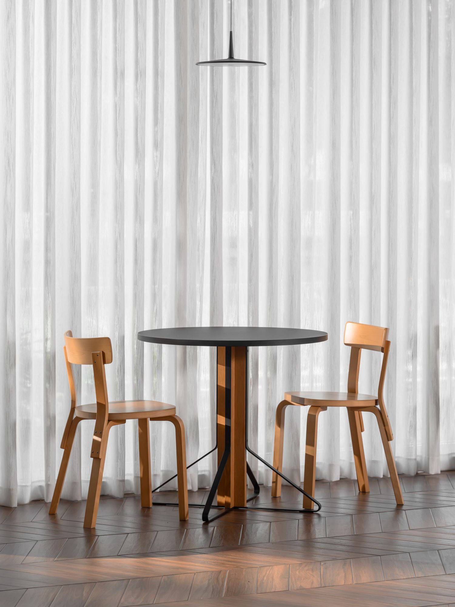 Round black table with two wooden chairs against a white curtain background