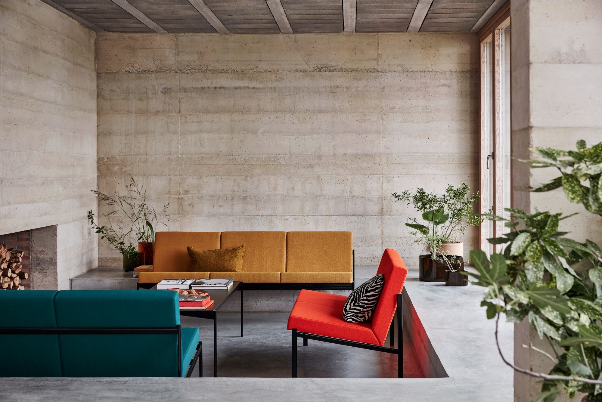 Modern living room with a yellow sofa, red chair, and green plants.
