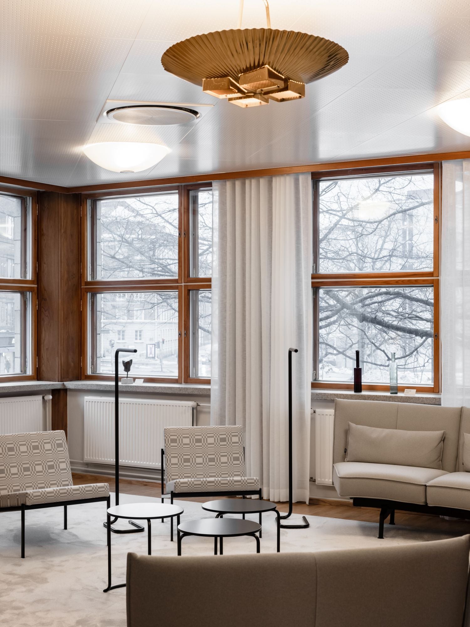 Modern living room with large windows, neutral furniture, and a gold chandelier.