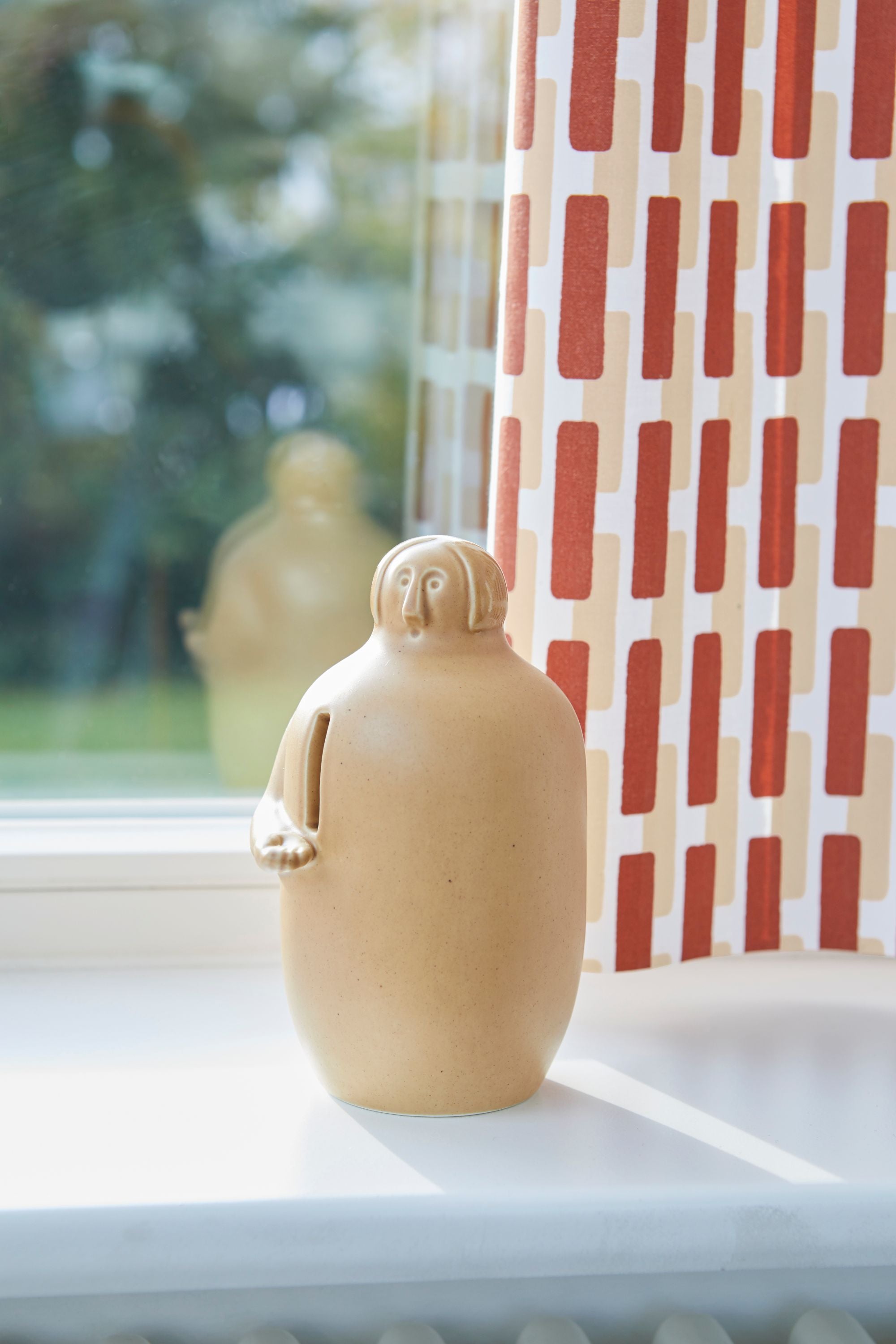 Beige ceramic jug on a windowsill with a red and white checkered curtain in the background