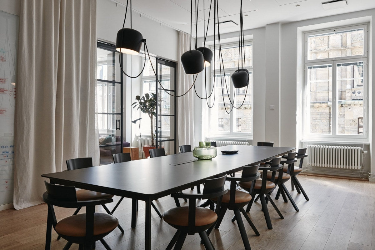 Modern conference room with long table and chairs, large windows, and hanging lights.