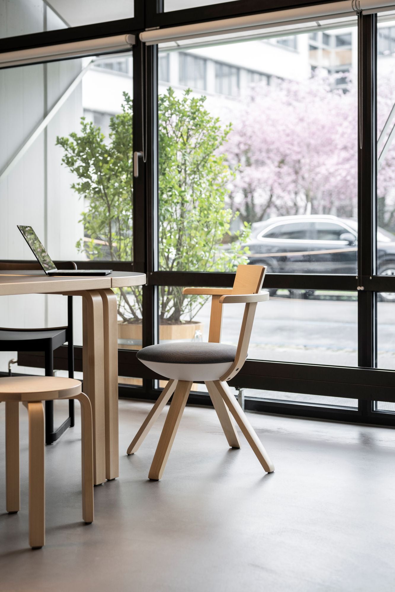 Modern interior with wooden chairs and tables near a large window with a cityscape view.