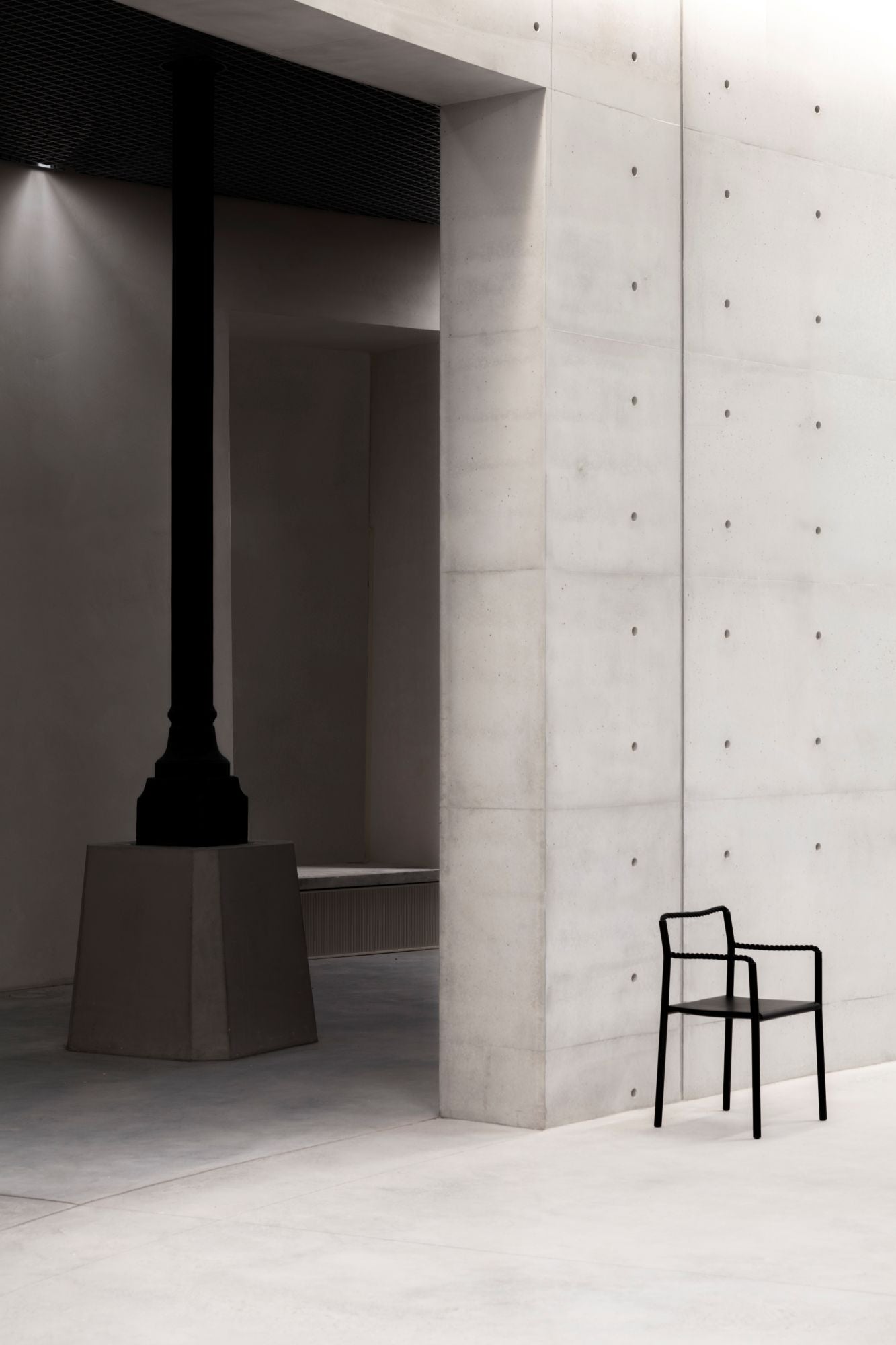 Modern black chair against a concrete wall with a dark cylindrical object.