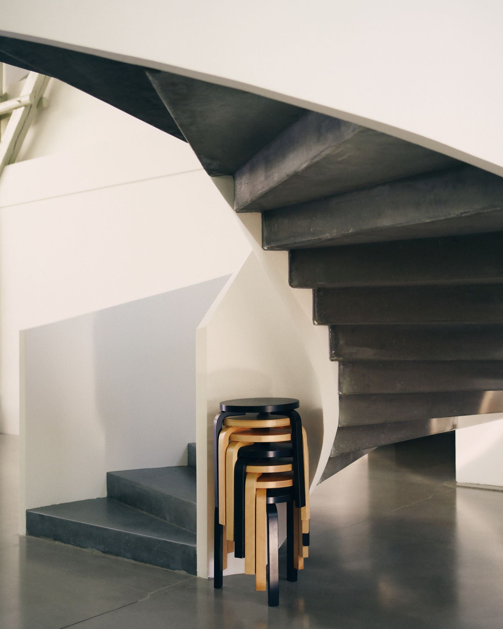 Modern staircase with a stack of stools against a white wall.