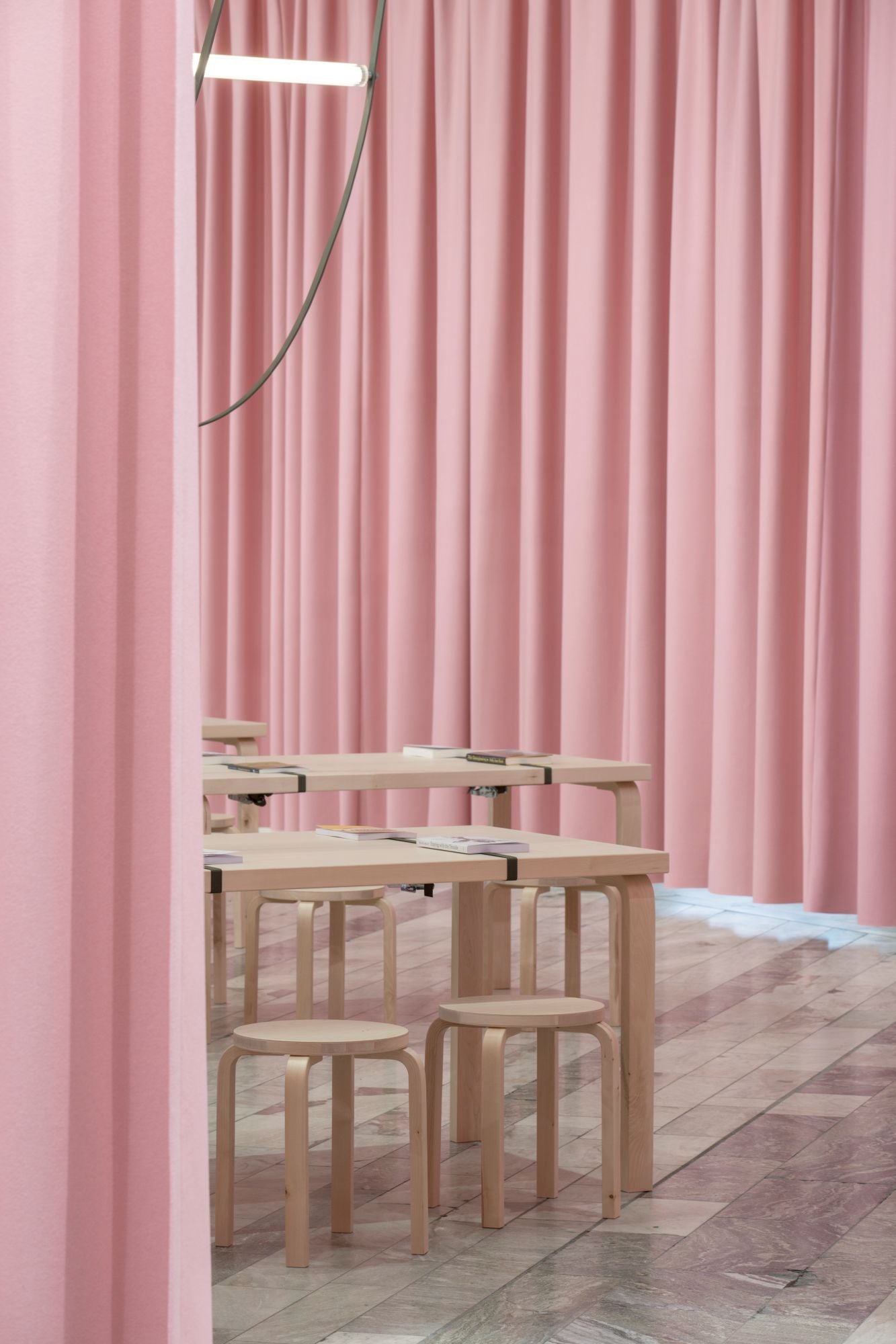 Wooden tables and stools against a pink curtain backdrop