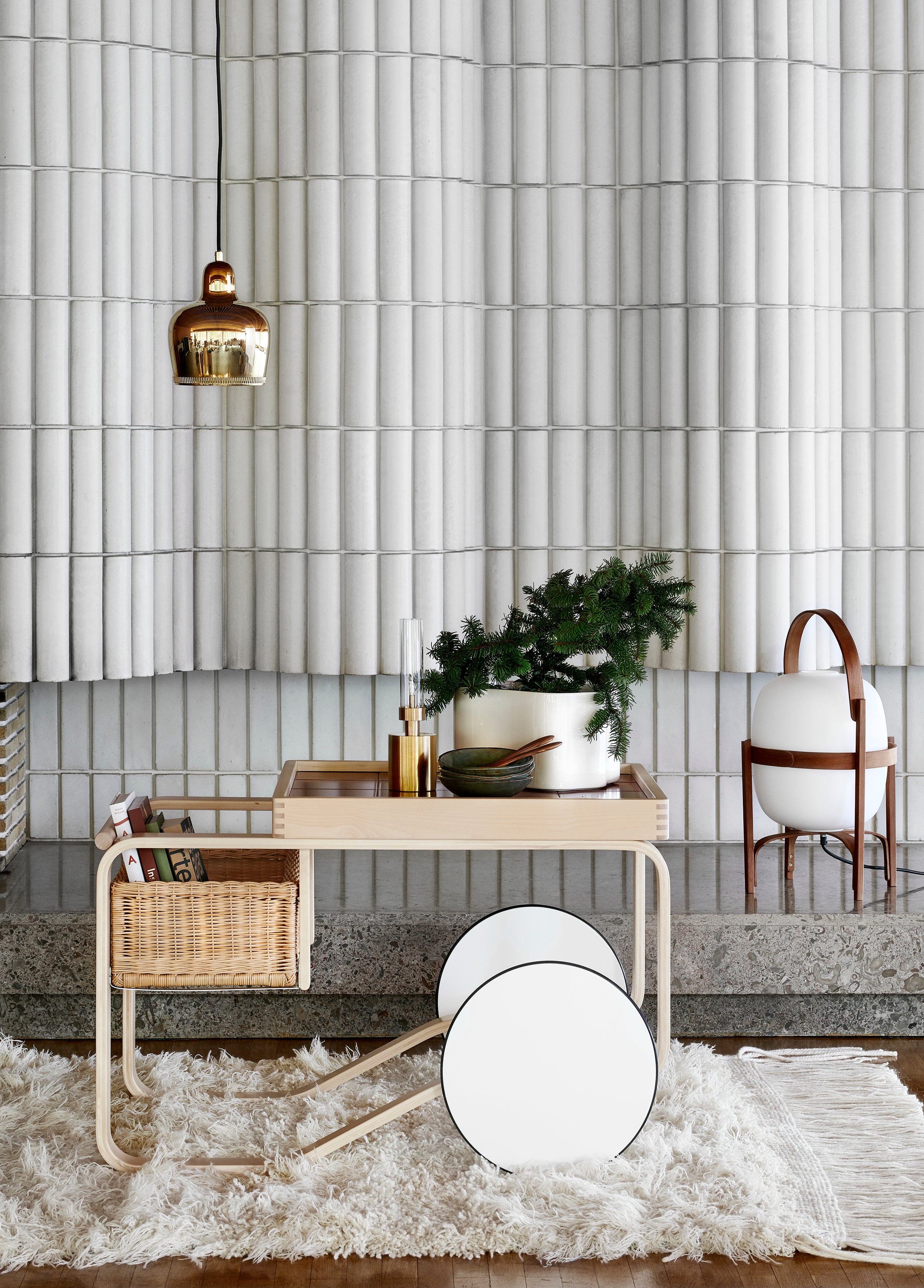 Modern interior with a light wood table, wicker basket, and decorative items against a tiled wall.