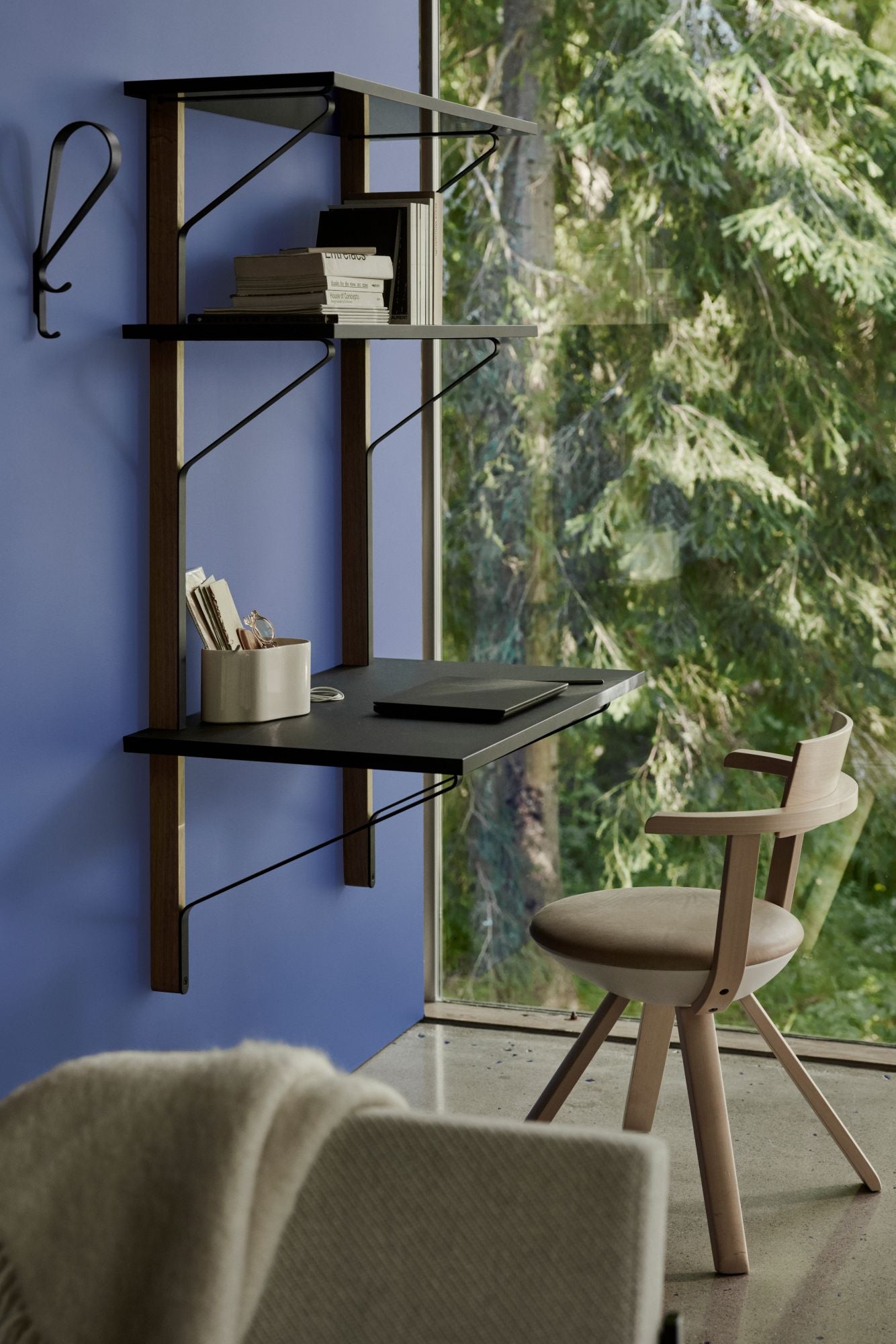 Wall-mounted desk with shelves against a blue wall with a large window showing greenery.
