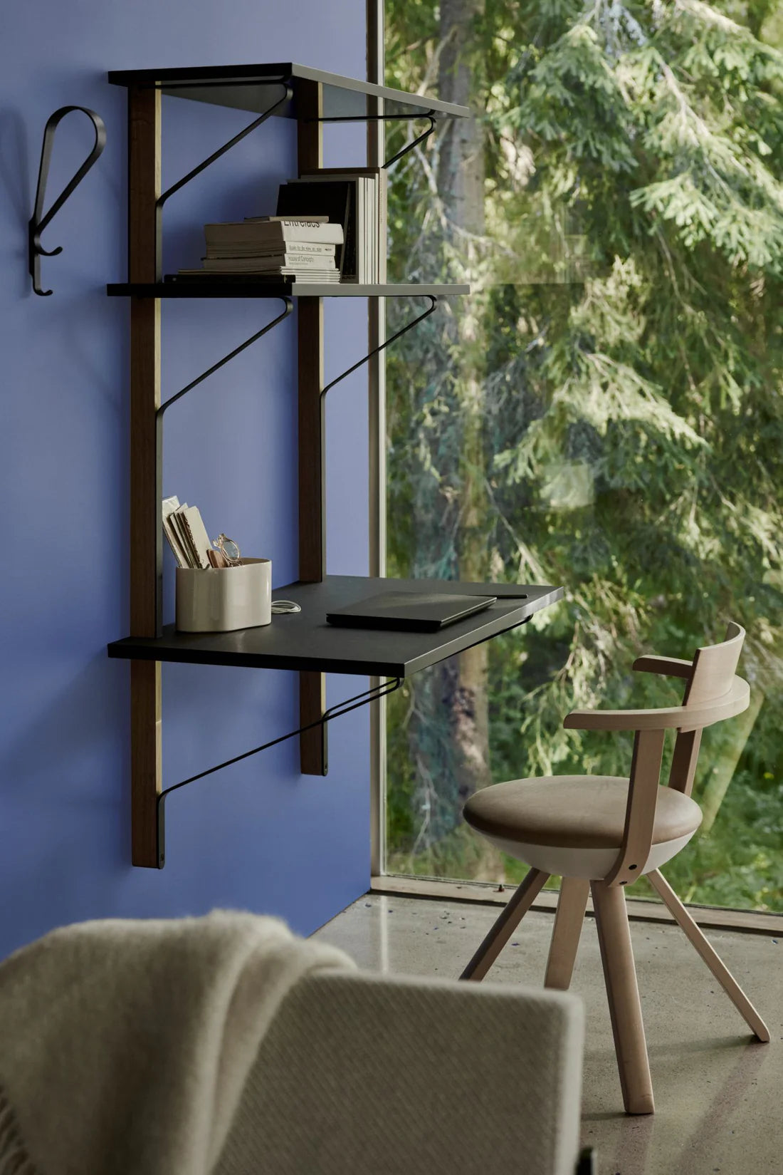 Wall-mounted desk with shelves against a blue wall with a large window showing greenery.