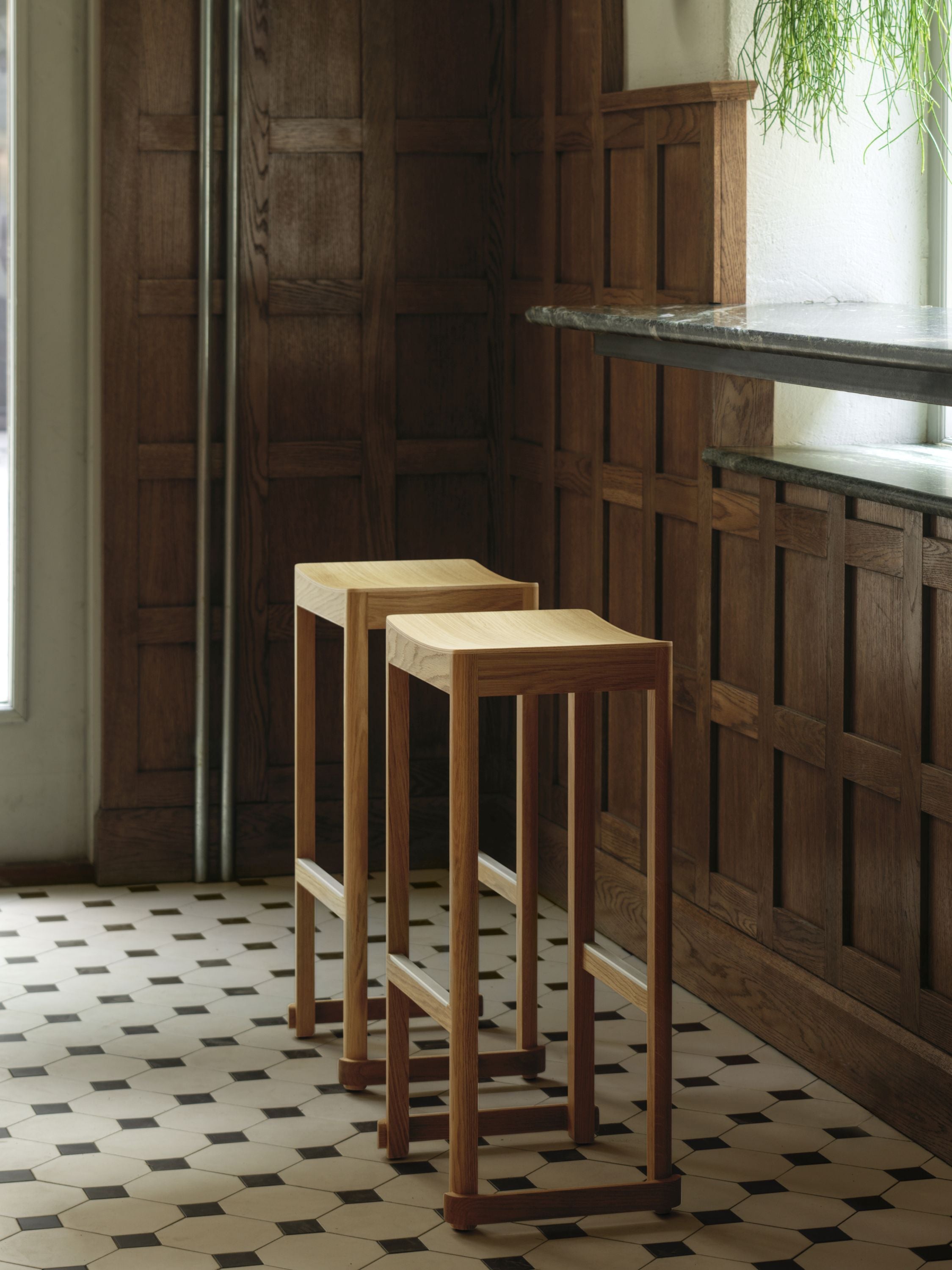 Two wooden stools in a room with wooden paneling and a tiled floor.
