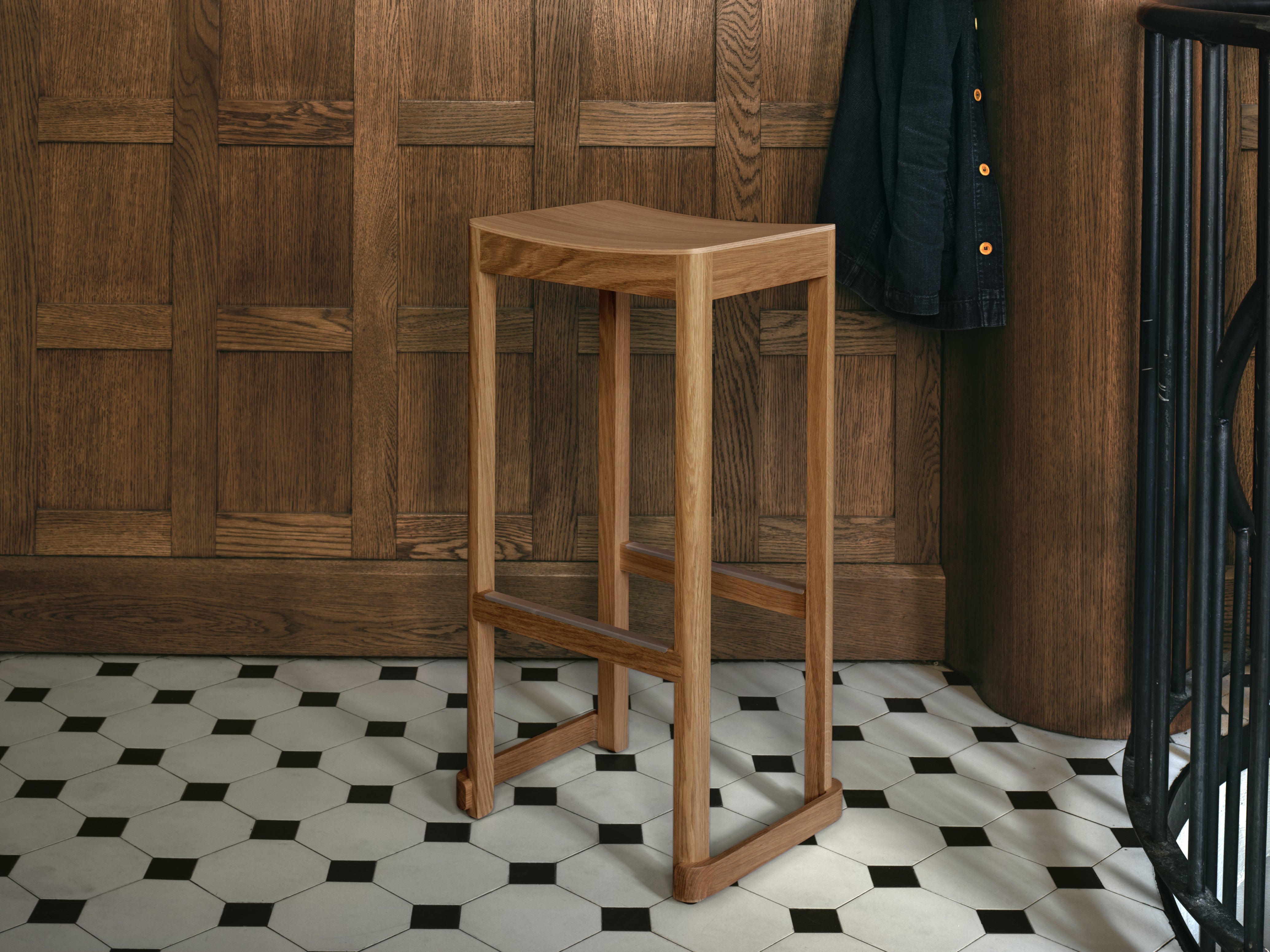 Wooden bar stool against a wooden paneled wall with a black and white tiled floor.