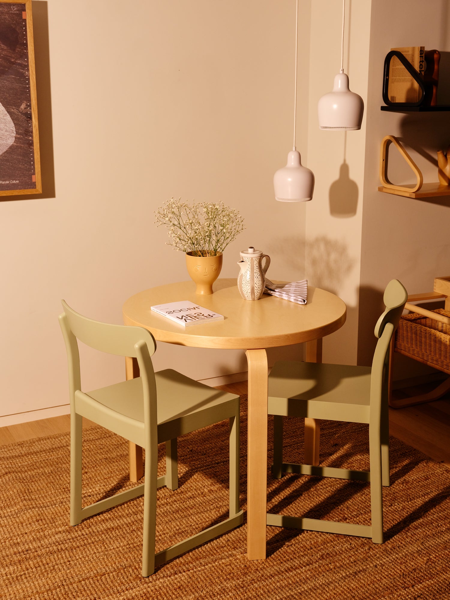 Round wooden table with two green chairs in a room with beige walls and a textured rug.
