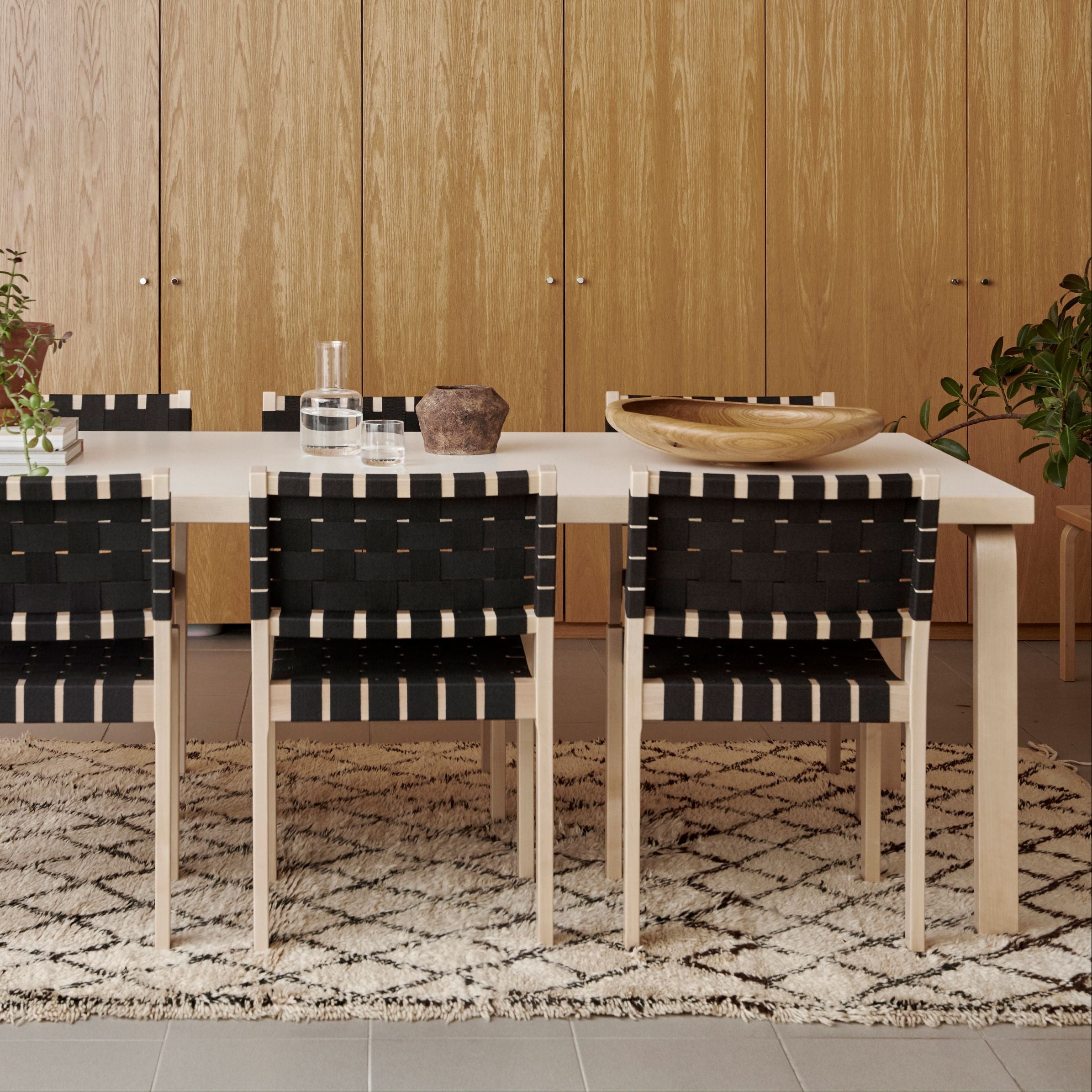 Dining table with black and white striped chairs in a room with wooden walls and a patterned rug.