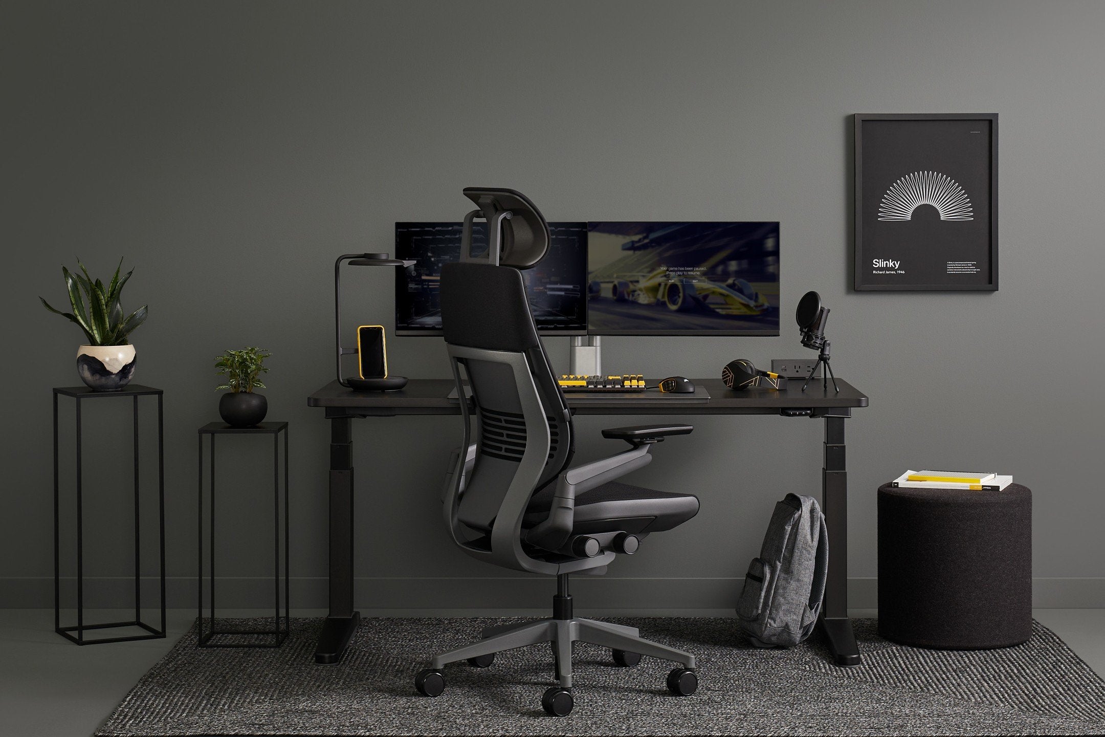 Modern home office setup with a desk, chair, and computer monitors against a gray wall.