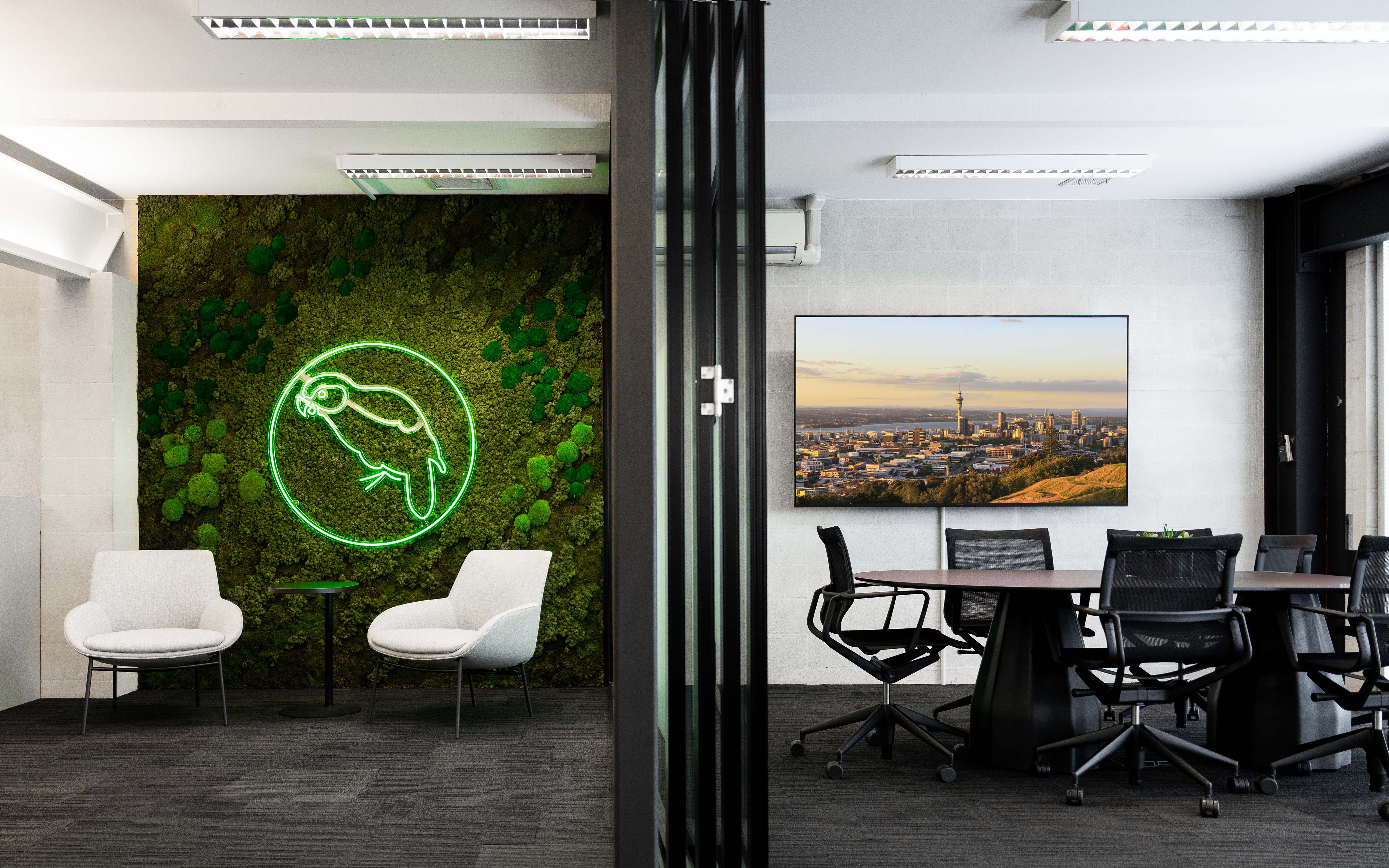 Modern office interior with a green neon sign on a wall and a conference room setup.