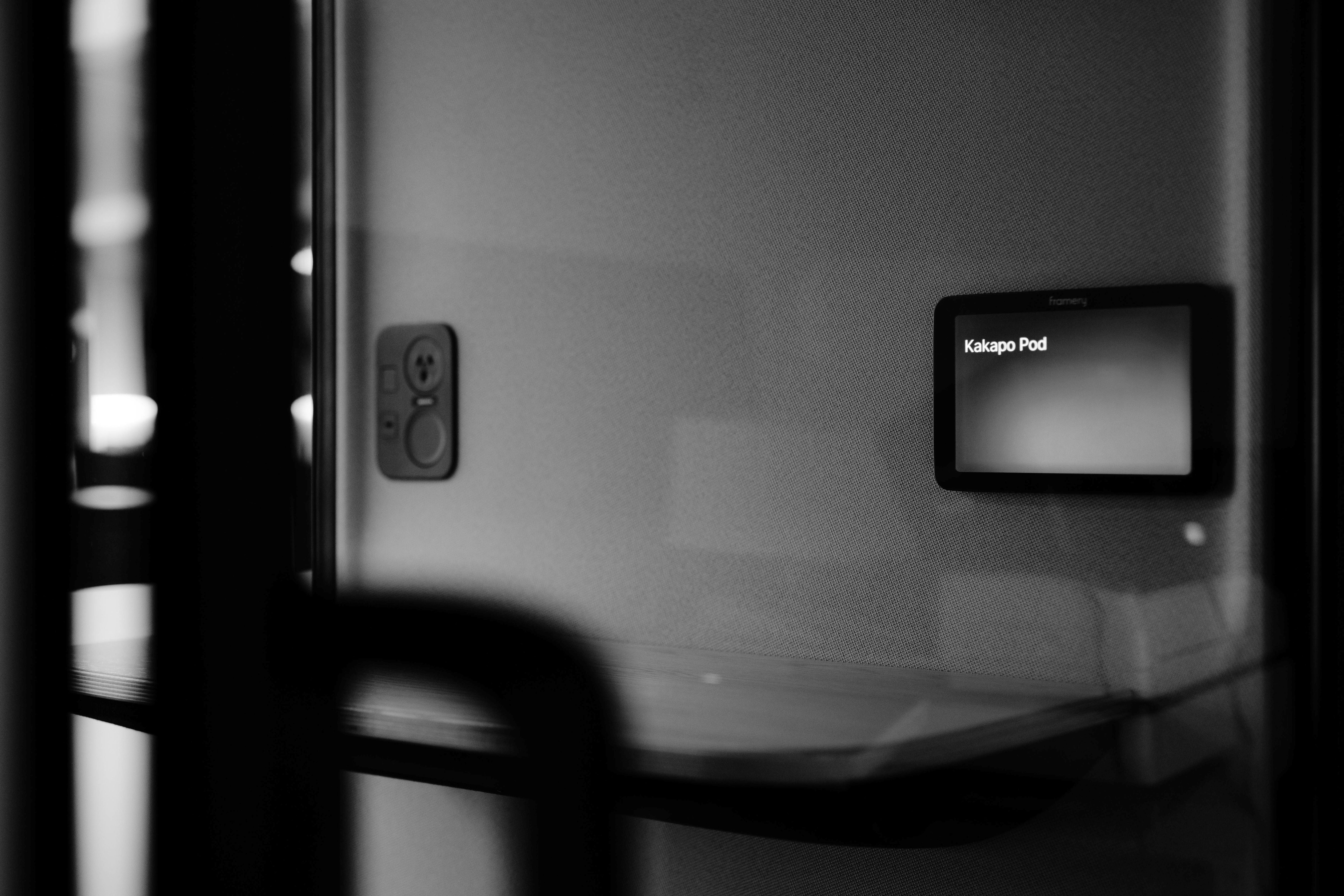 Black and white image of a device with a screen displaying 'Kakapo Pod' on a reflective surface.