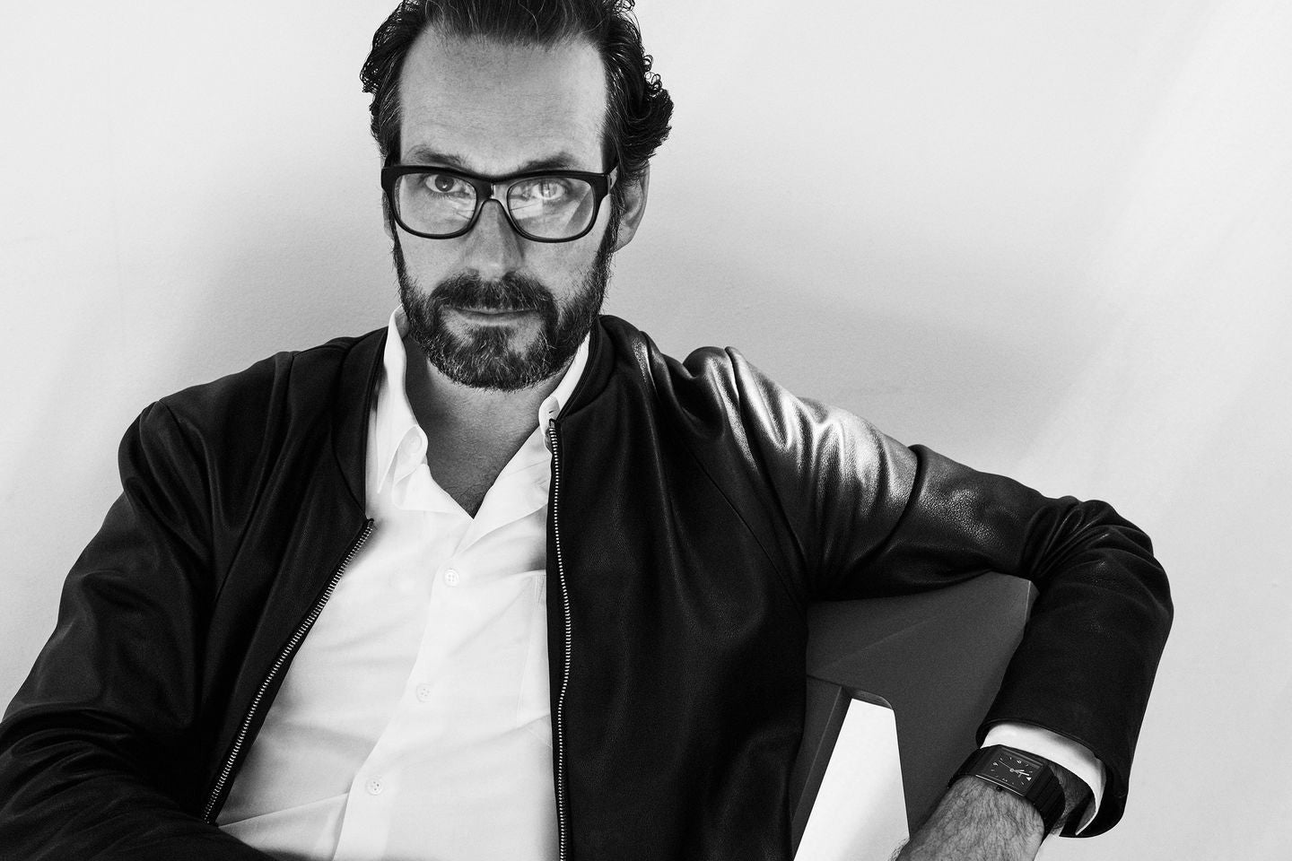 Man wearing glasses and a black jacket over a white shirt on a light background