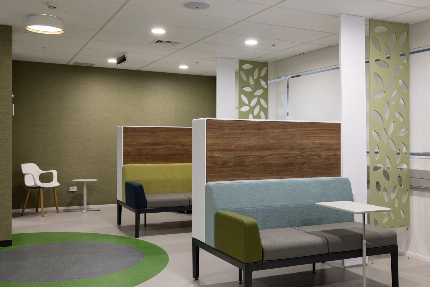 Modern office break room with green walls, wooden partitions, and seating area.