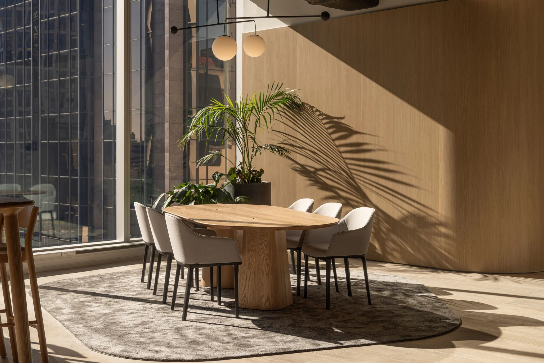 Dining area with a round wooden table and chairs near large windows with cityscape view.