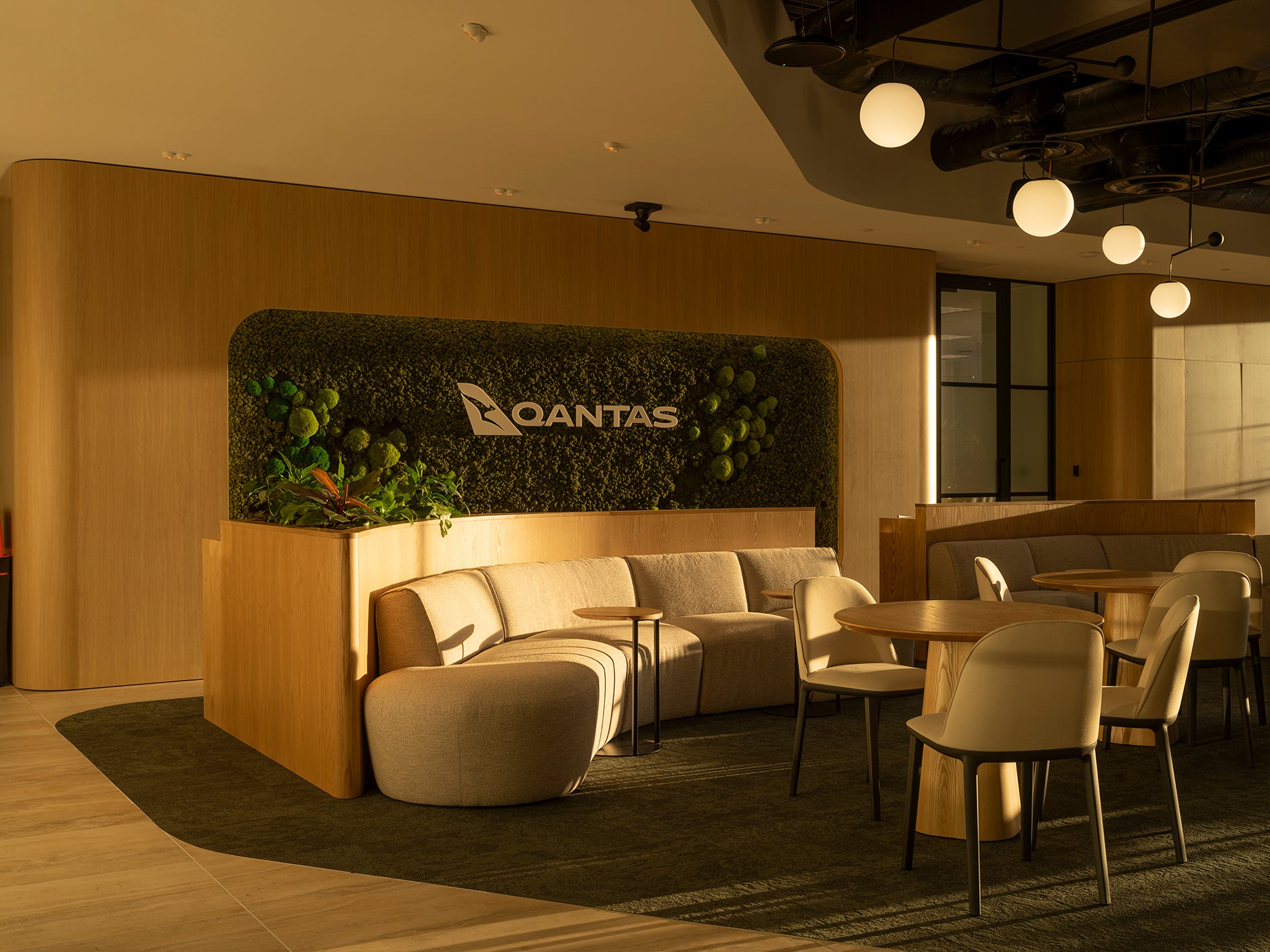Modern lounge area with Qantas branding, featuring seating and tables.