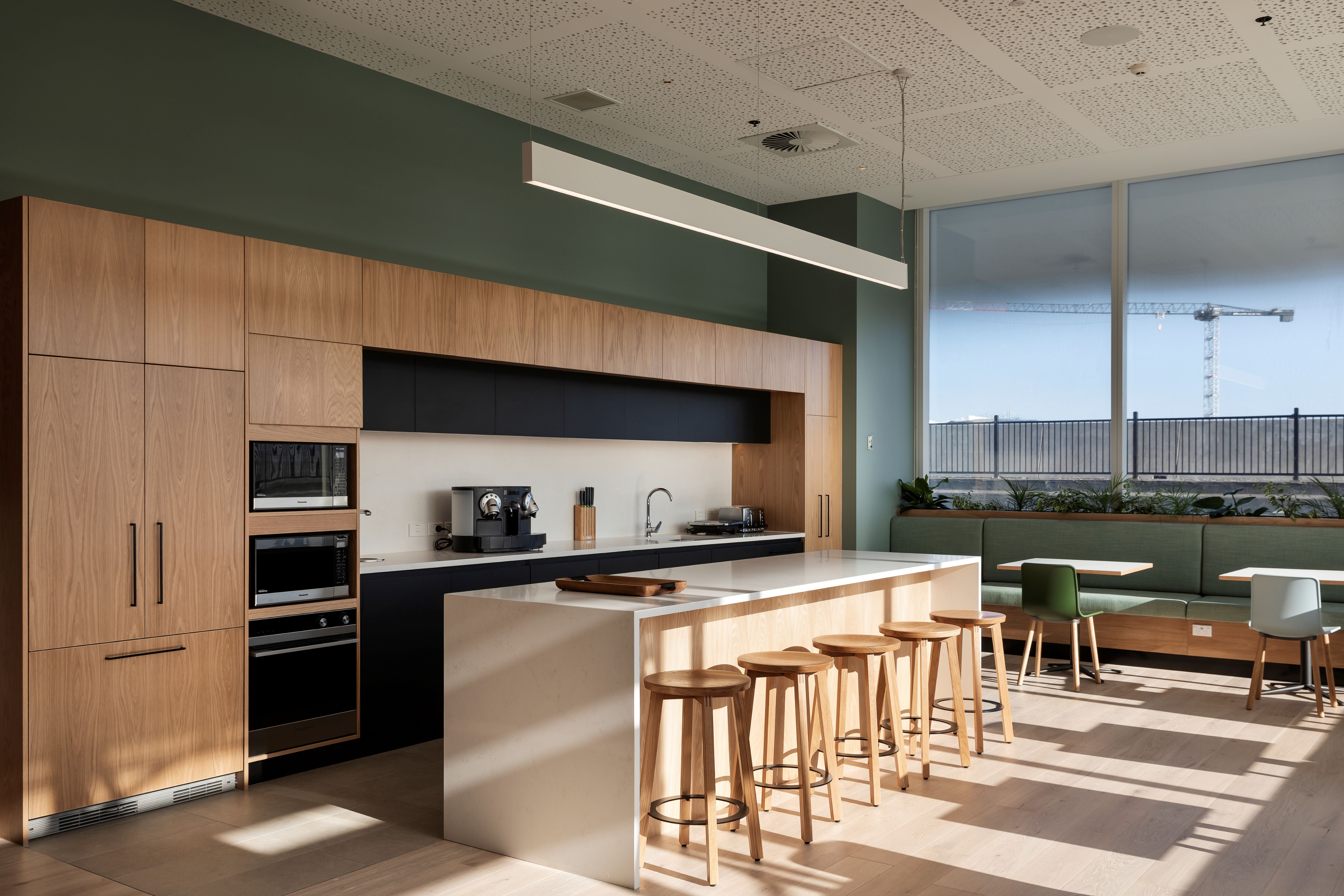Modern kitchen with wooden cabinets, island, and stools in a well-lit room.