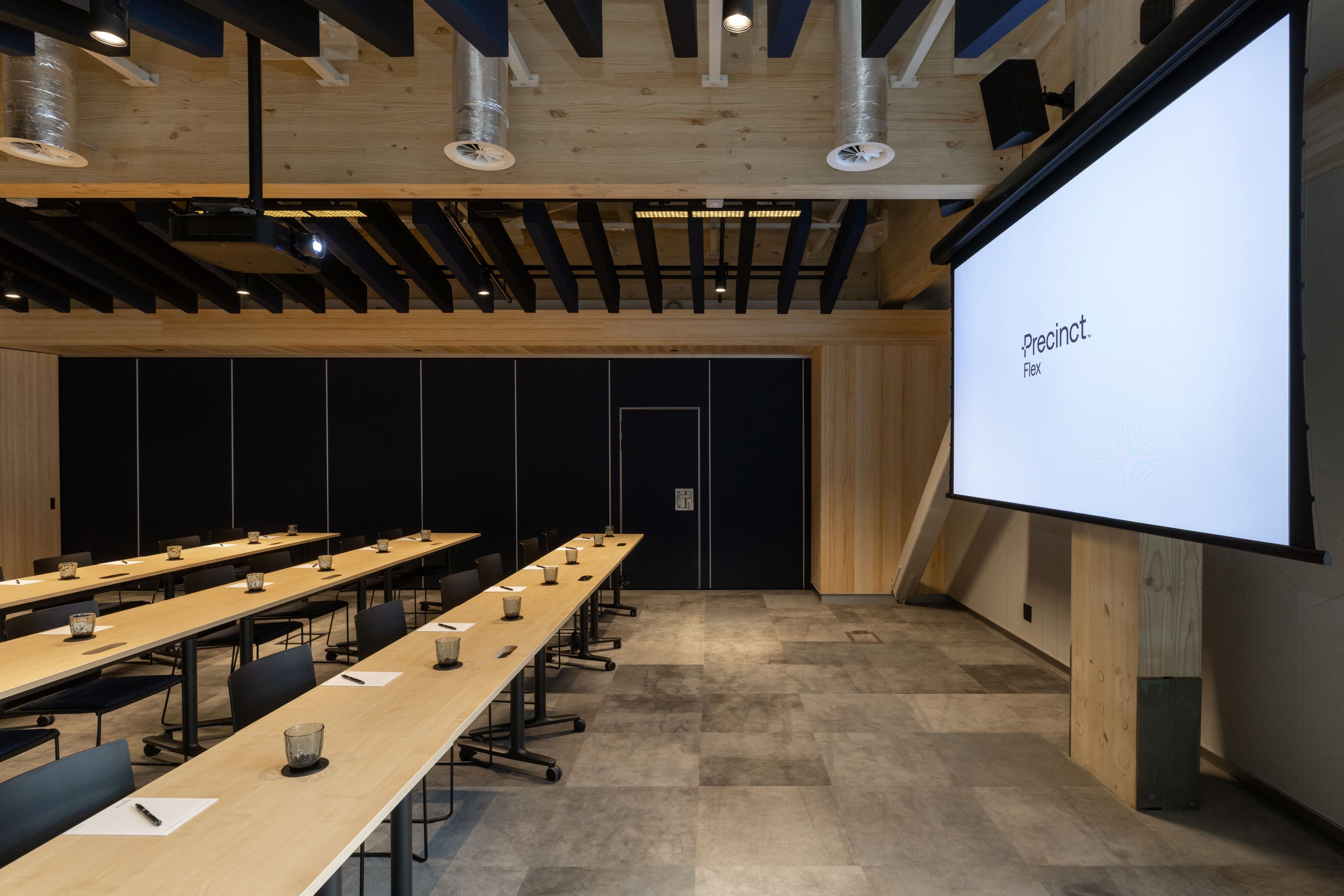 Modern conference room with long wooden tables and a large screen displaying 'Proecto'.