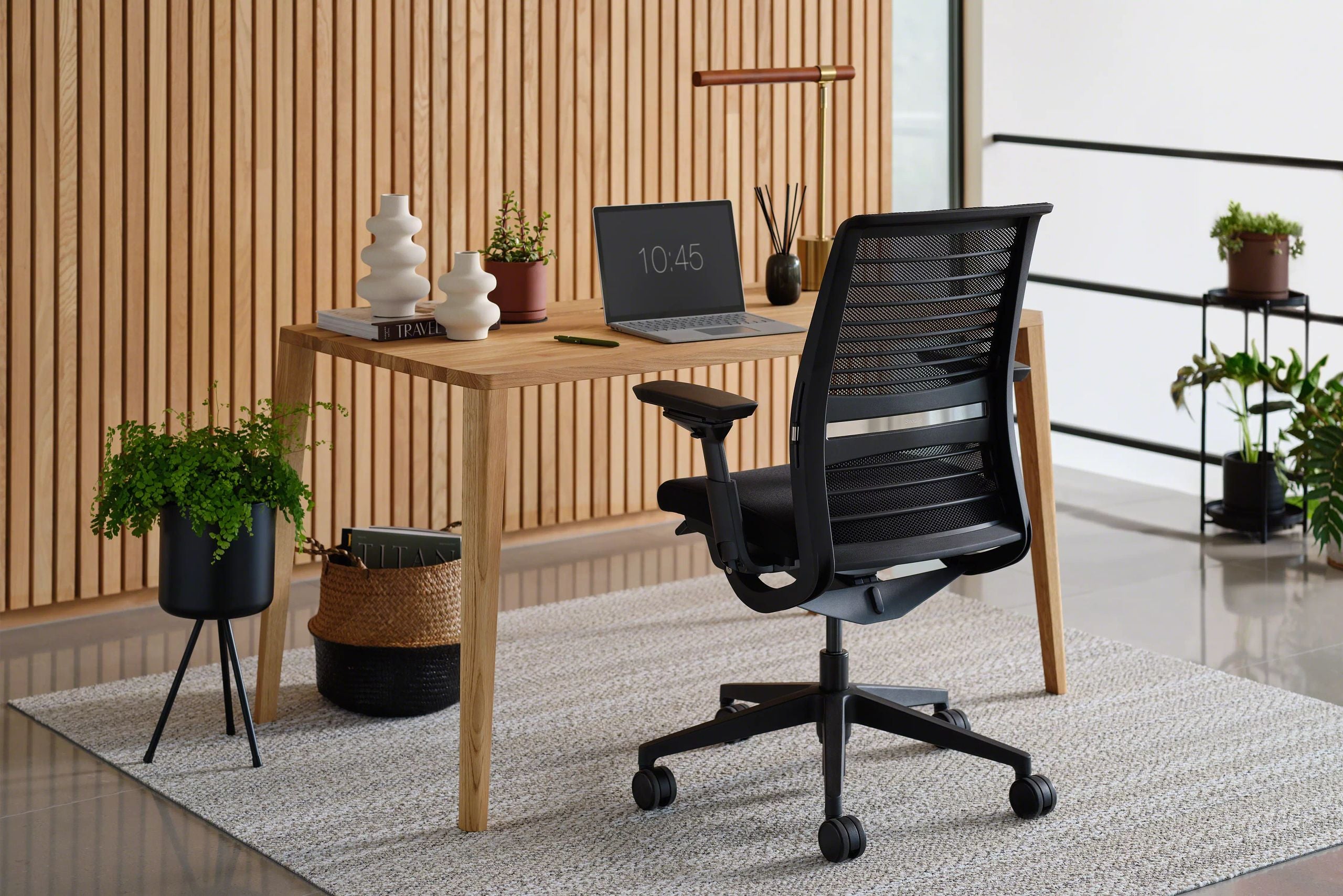 Modern office desk with black chair, plants, and decor in a bright room.