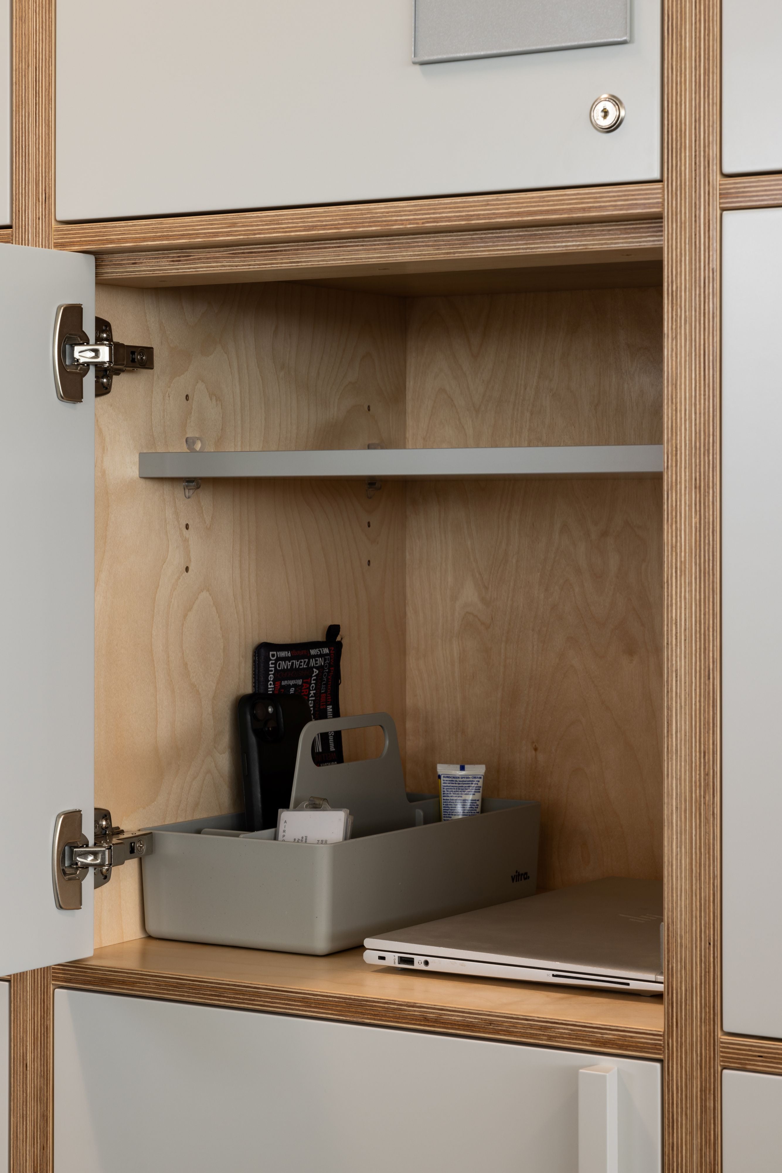 Wooden cabinet with open door showing a gray organizer, laptop, and other items.