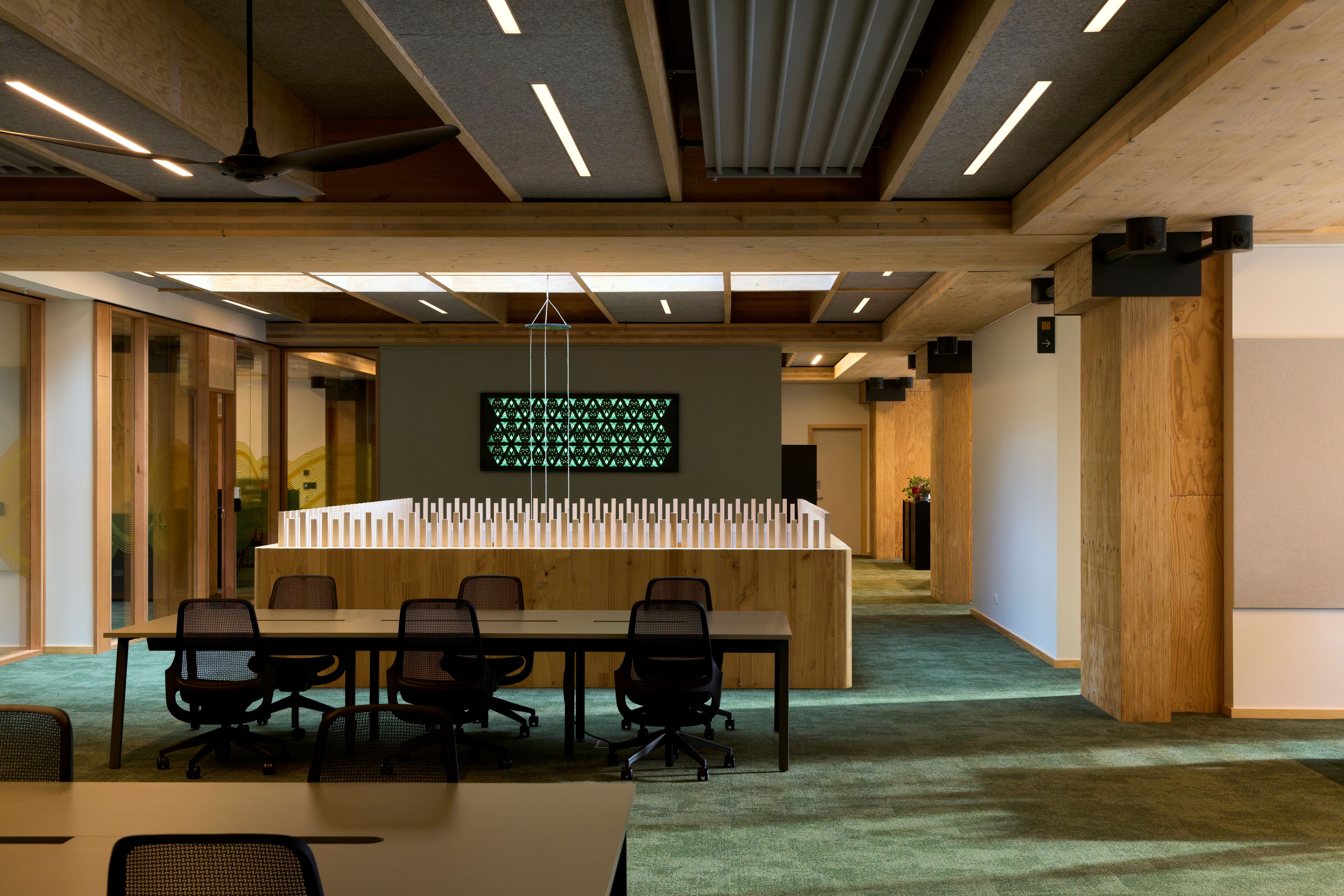 Modern office space with a large meeting table and chairs, digital display on the wall.
