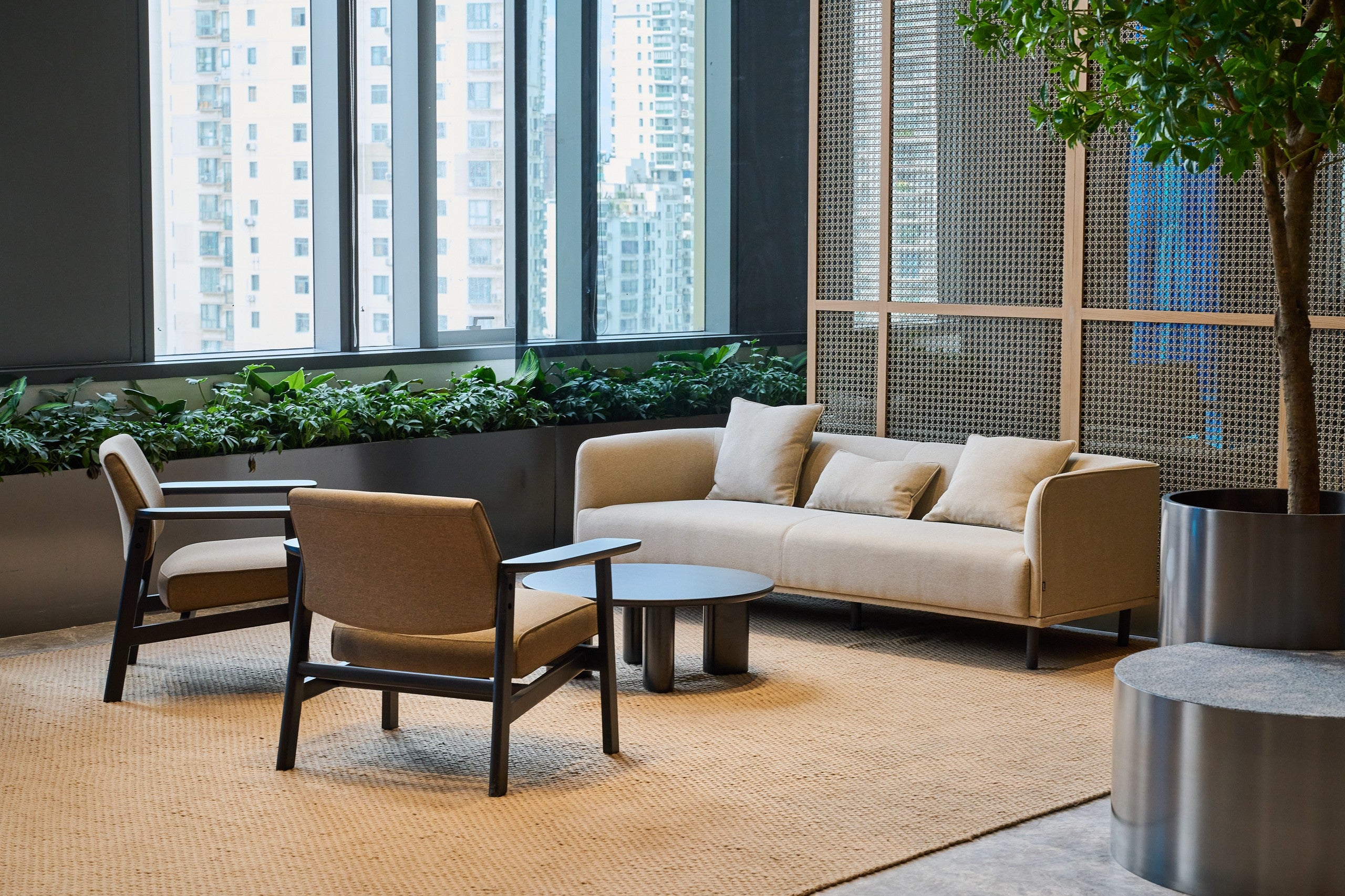 Modern indoor setting with beige sofa, chairs, and coffee table near large windows with cityscape view.